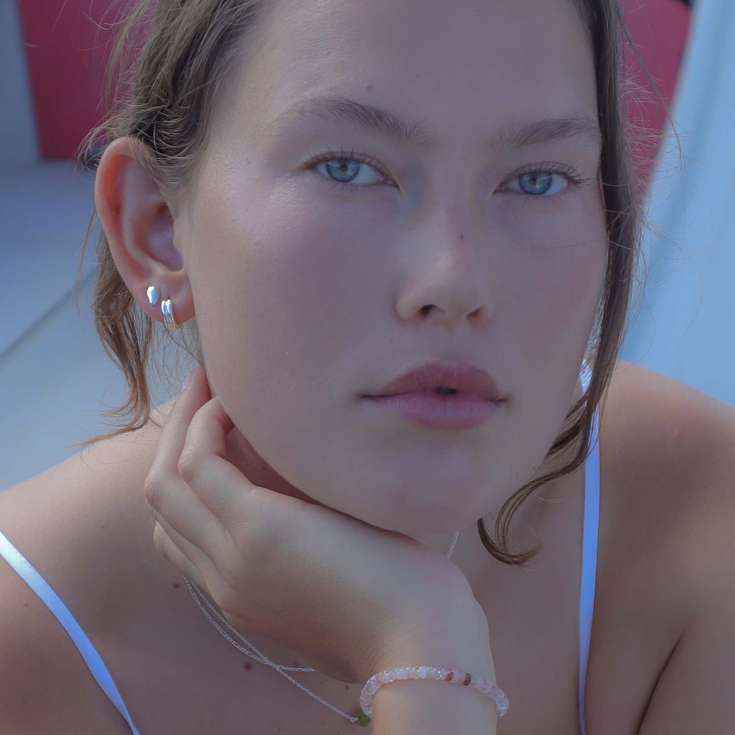 Close-up of a person with a hand on their chin, wearing earrings and a necklace.