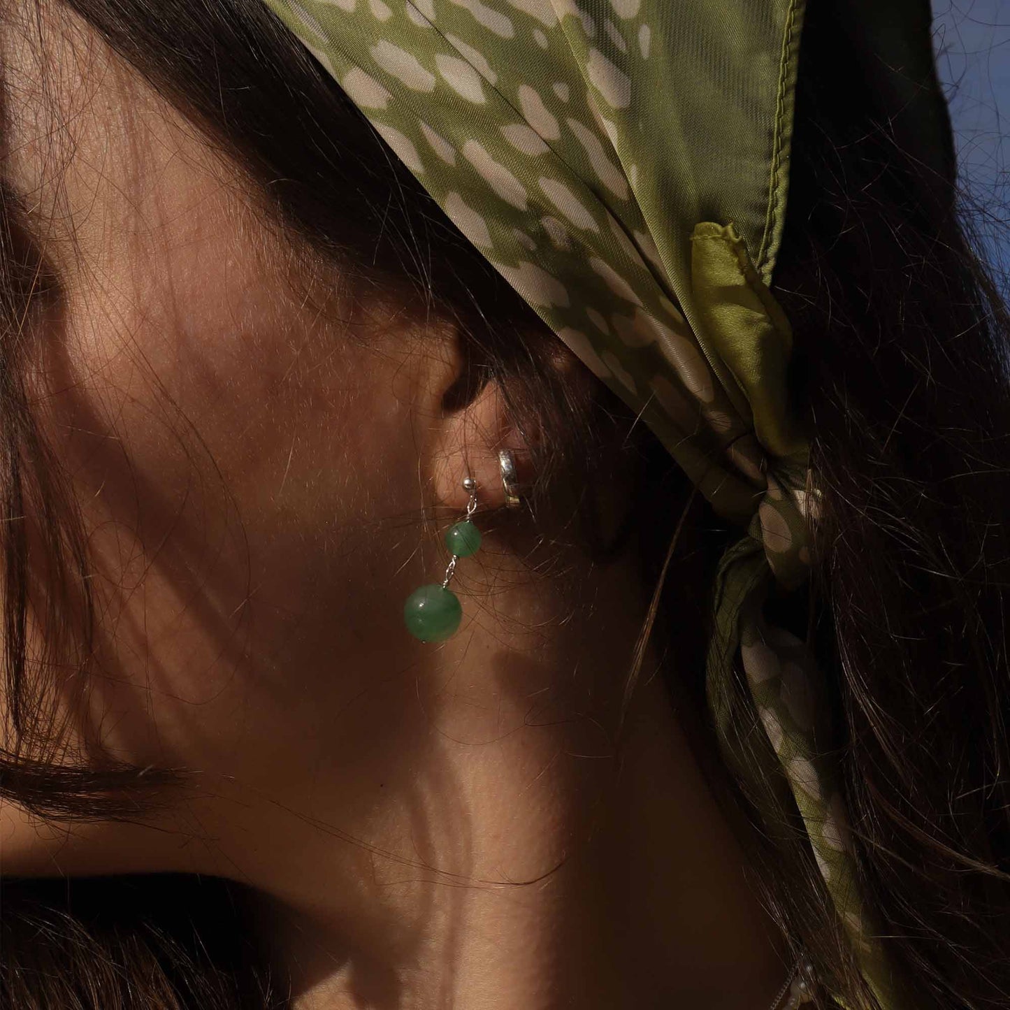Close-up of an ear with green earrings and a green headscarf.