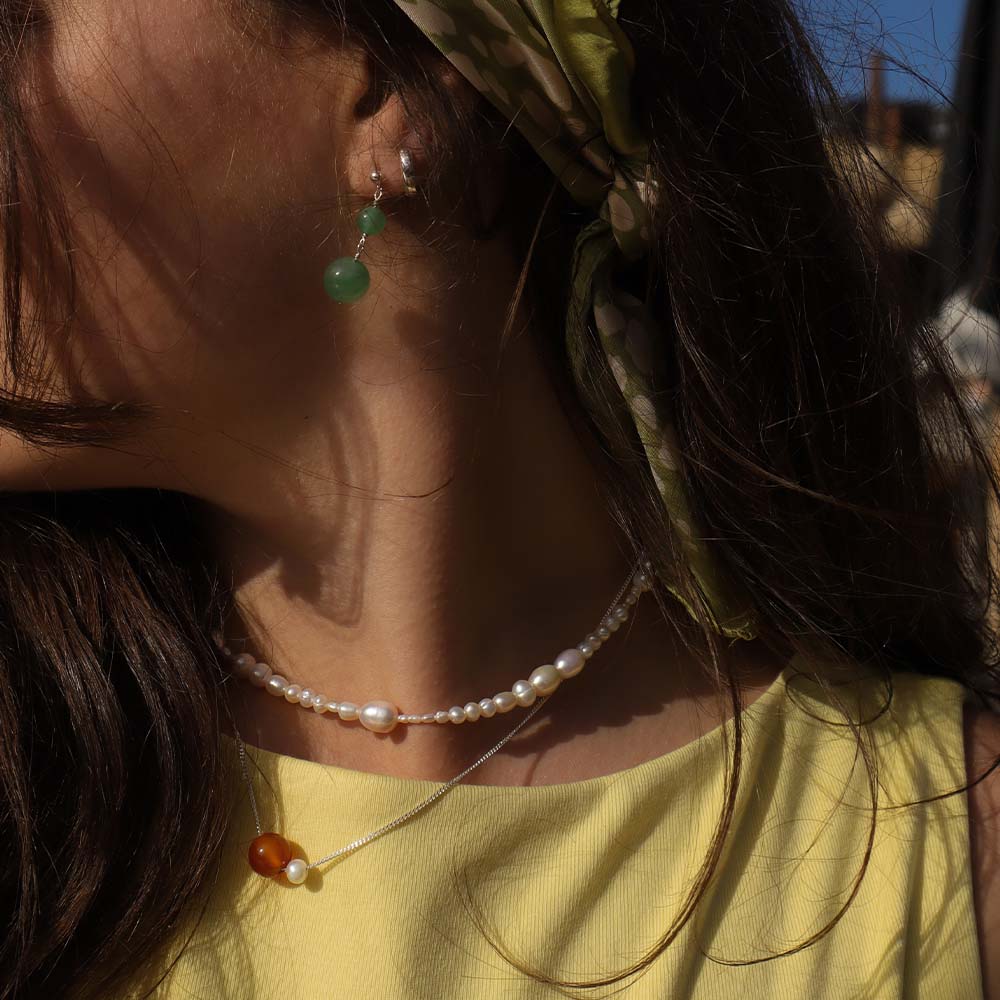 Close-up of a person wearing a yellow top and pearl necklace with green earrings.