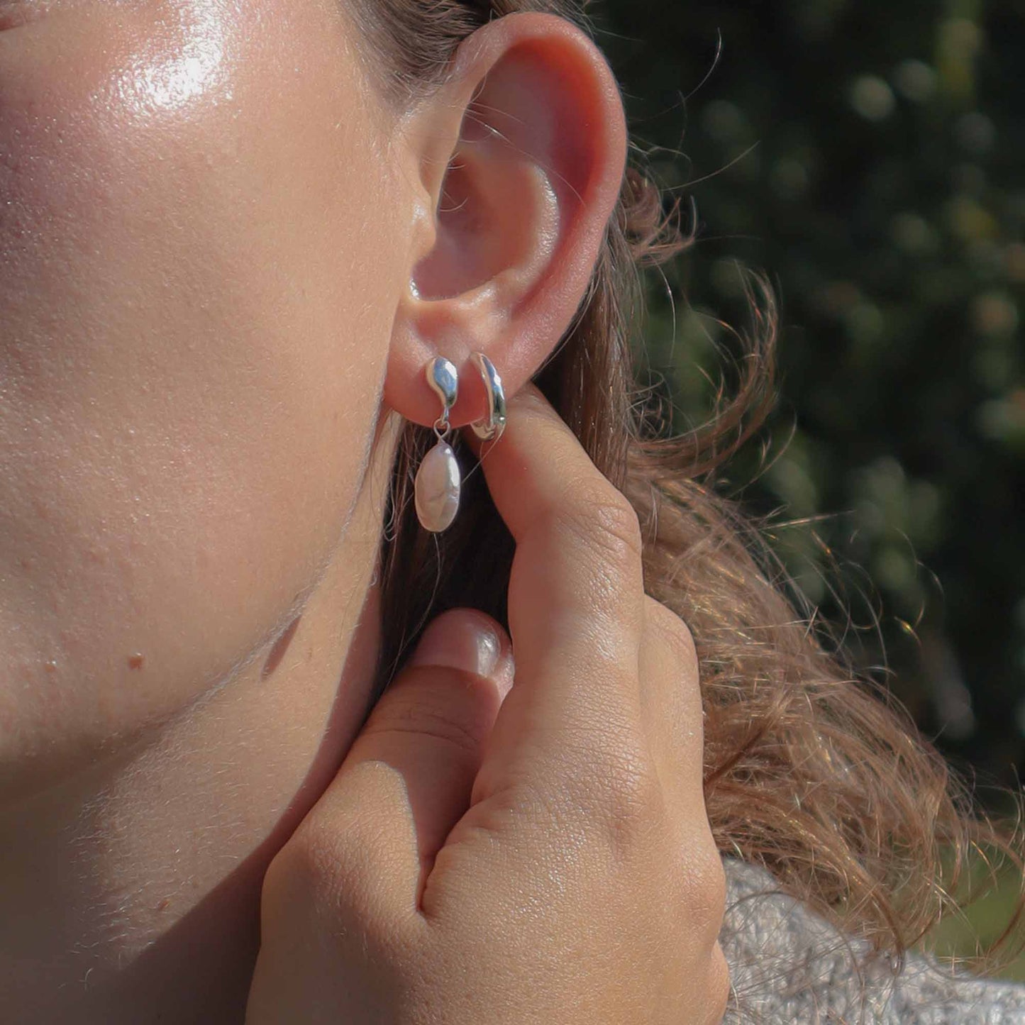 Close-up of a person wearing silver hoop earrings with a blurred natural background