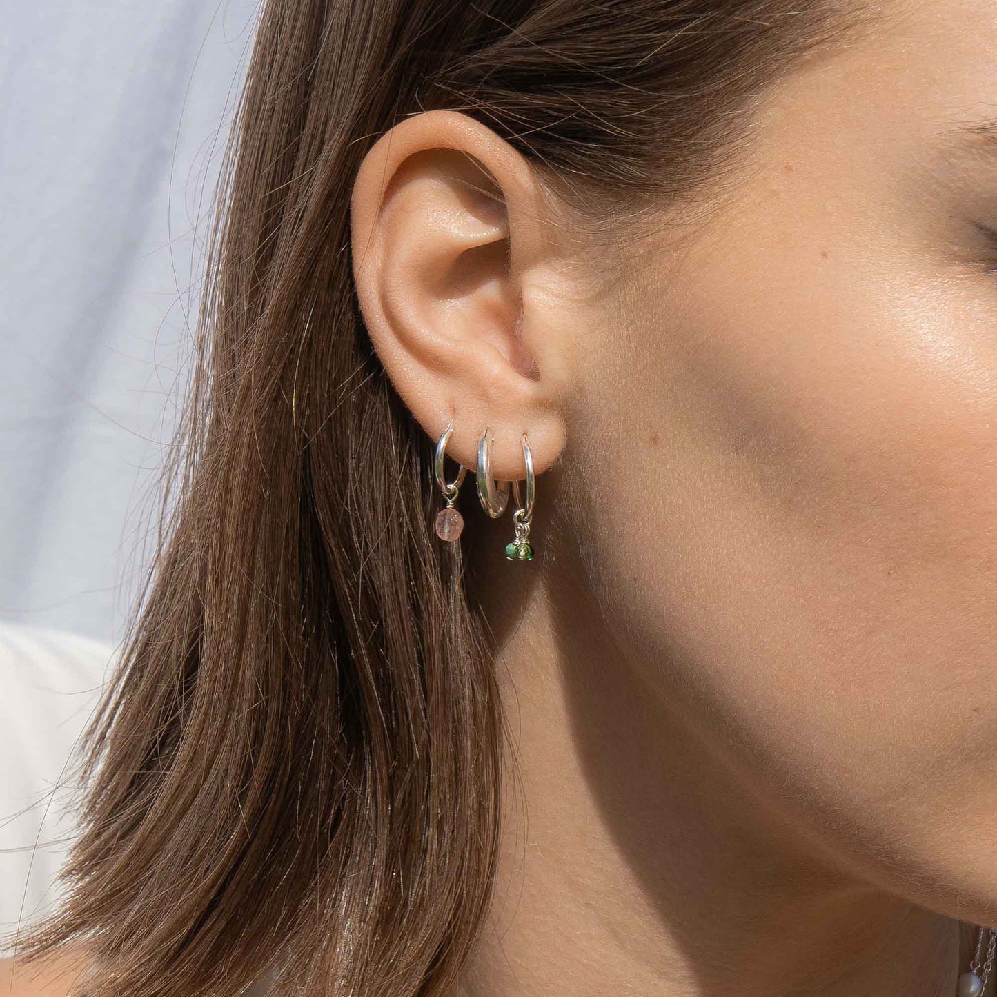 Close-up of a person wearing multiple hoop earrings with small charms.