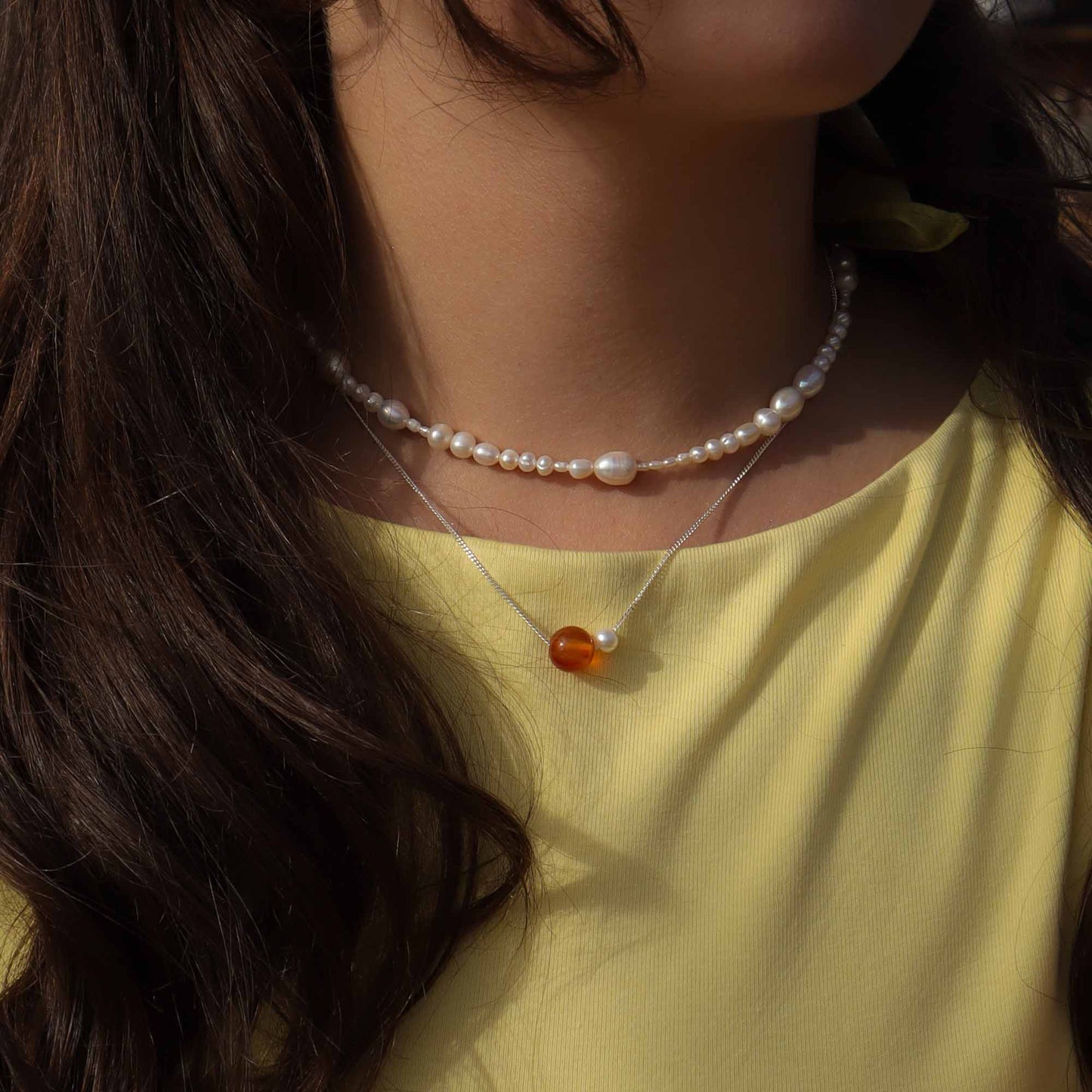 Close-up of a person wearing a pearl necklace with an amber pendant on a yellow background
