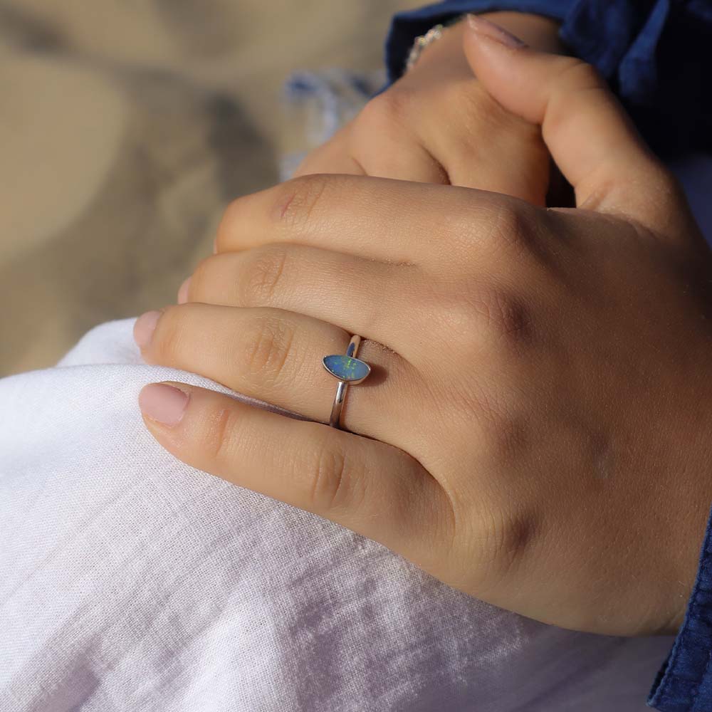 Close-up of a hand wearing a silver ring with a blue stone on a blurred background
