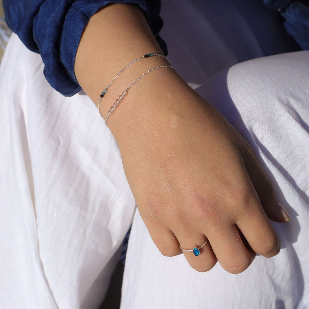Hand wearing a ring with a blue stone on a white fabric background