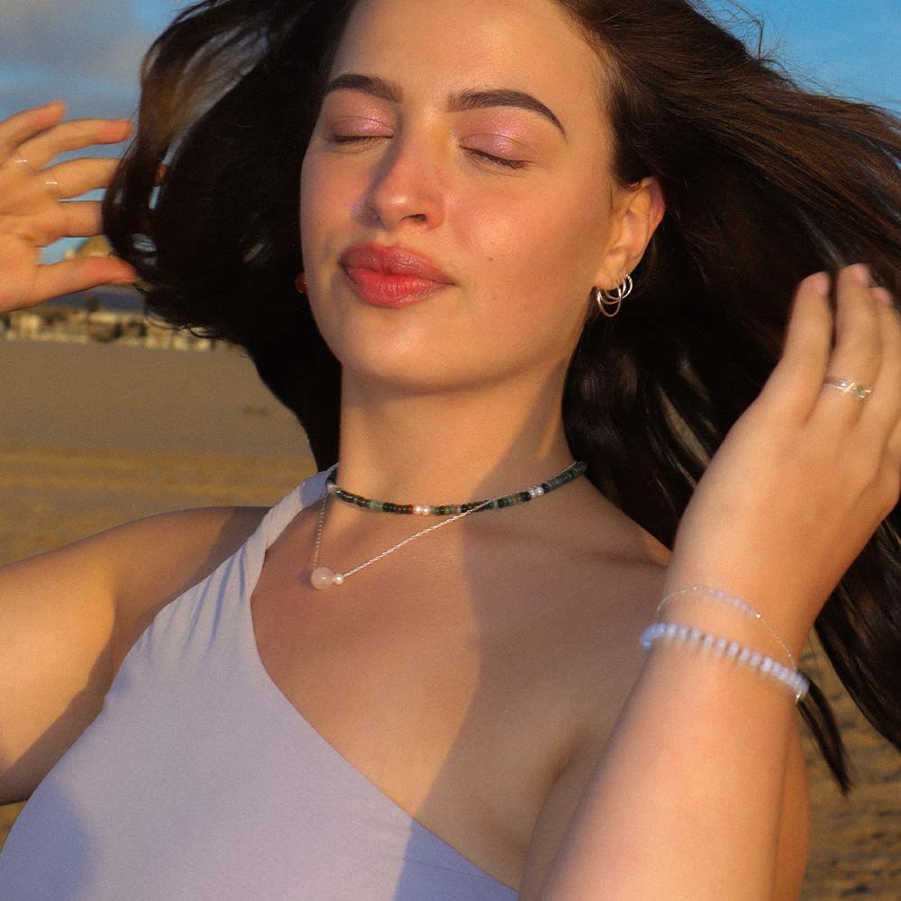 Woman with closed eyes on a beach, hands in her hair