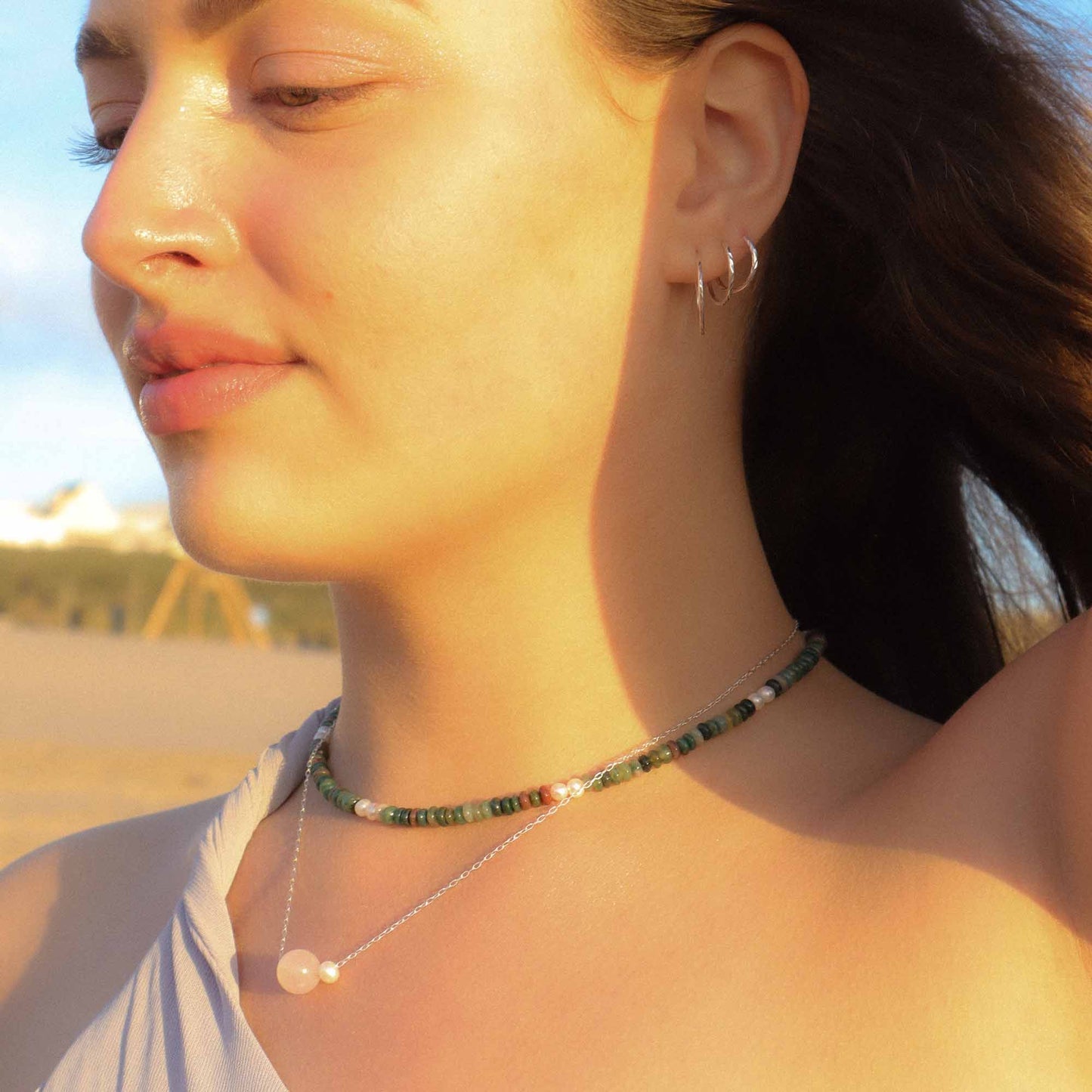 Woman wearing a necklace and earrings with a blurred outdoor background