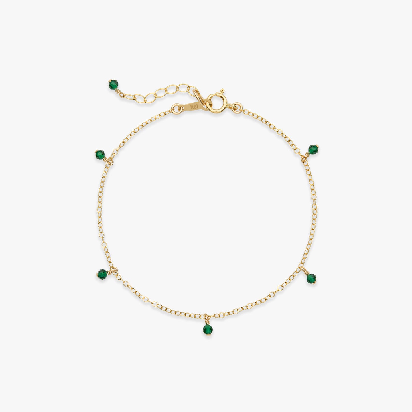 A delicate gold chain bracelet with small green bead accents spaced along the chain, displayed on a clean white background.
