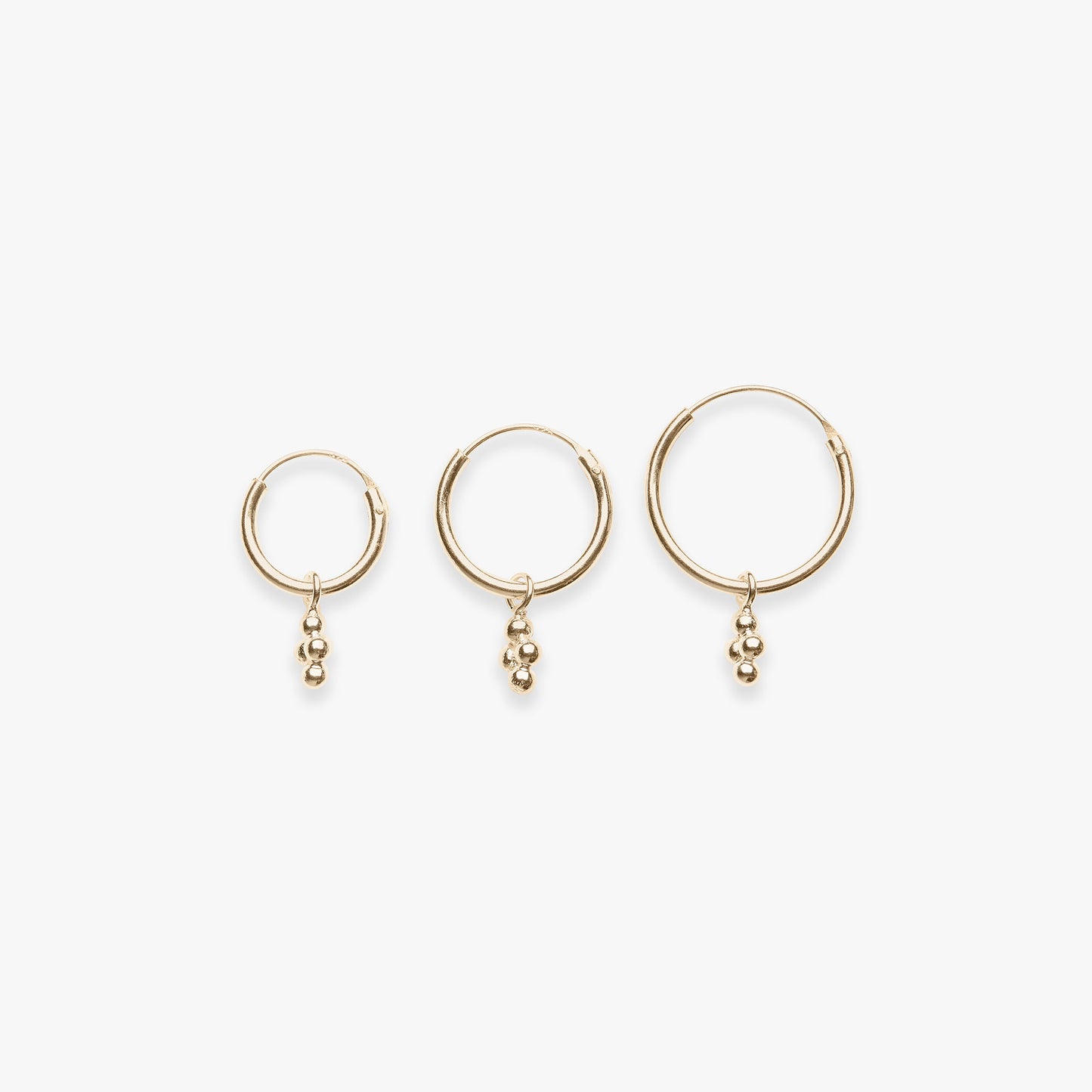 Three gold hoop earrings with small dangling beads on a white background