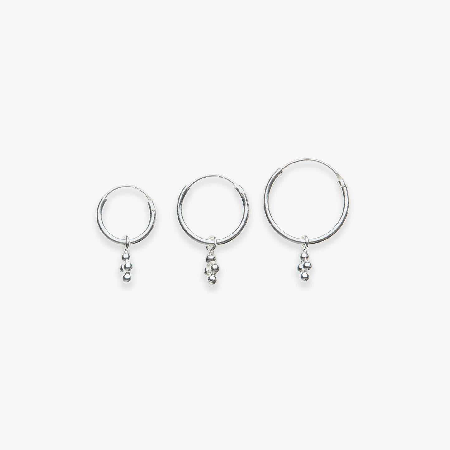 Three silver hoop earrings with small dangling beads on a white background