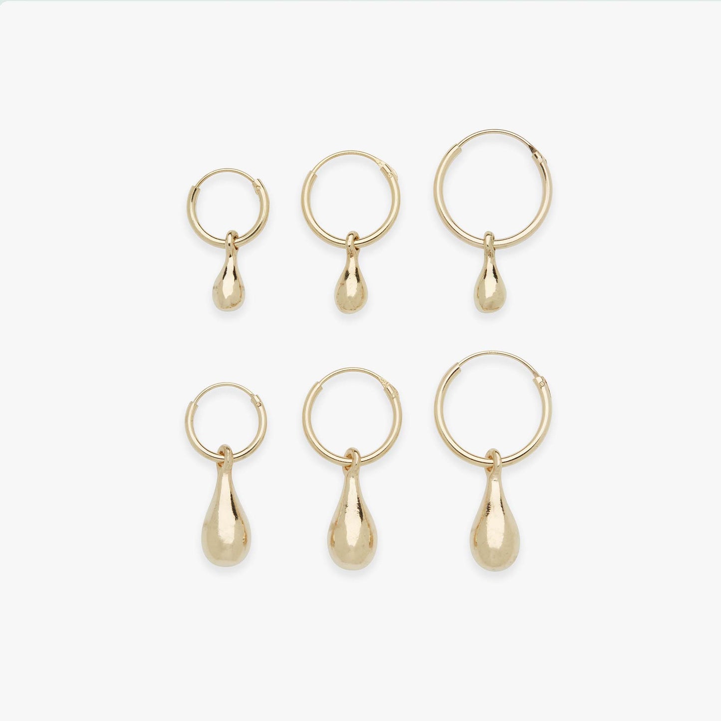 Set of gold hoop earrings with teardrop pendants on a white background