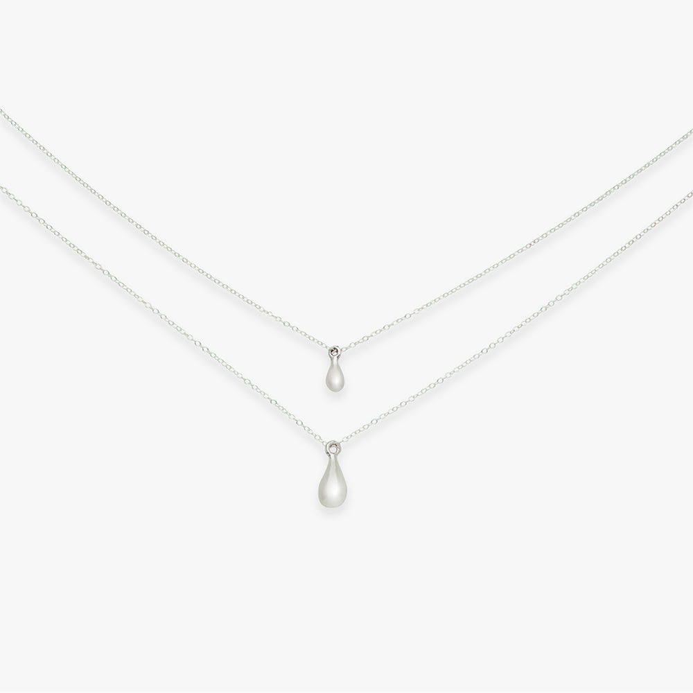 Two teardrop pendants on silver chains against a white background
