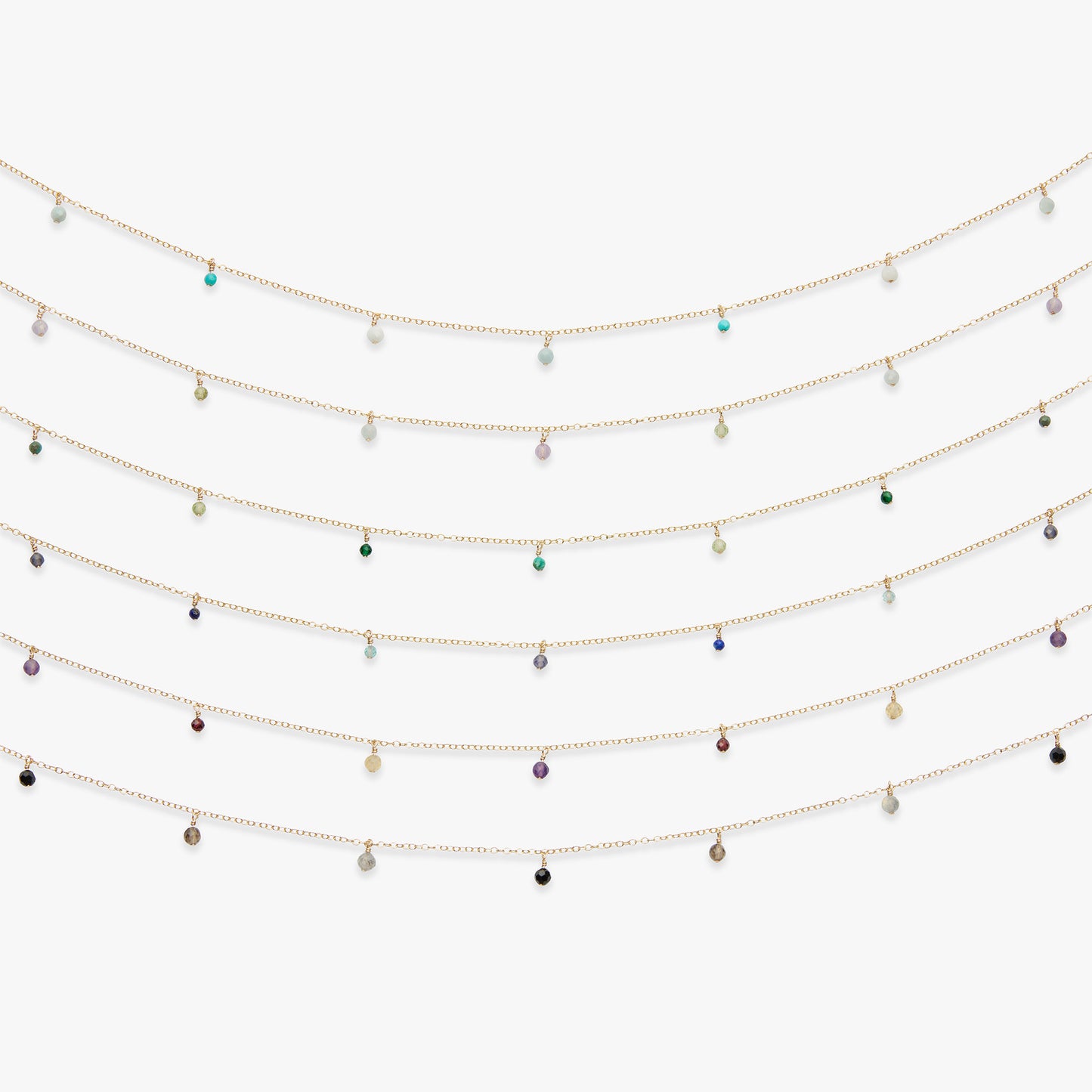 Five delicate gold chain necklaces with small dangling teardrop charms in assorted colors, arranged in a curved row against a plain white background.