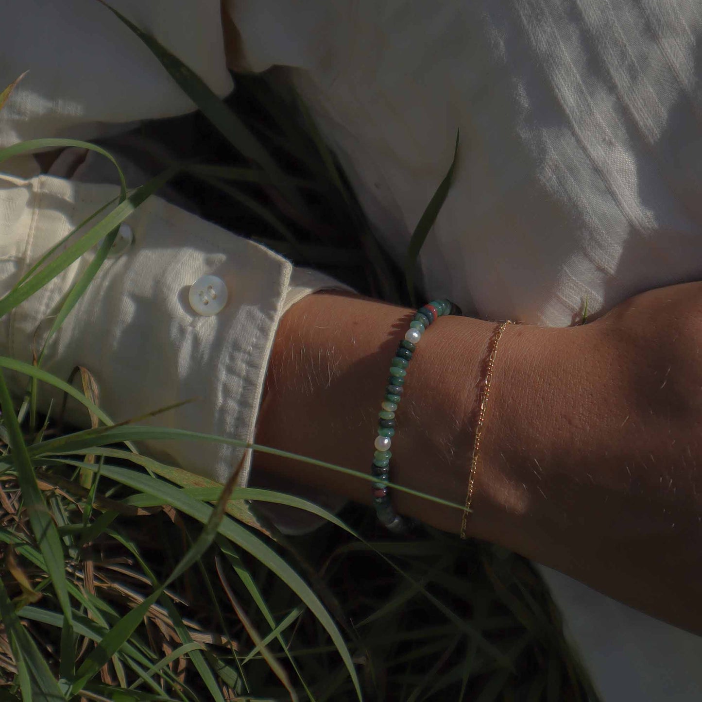 Person wearing a bracelet with grass and a white shirt in the background