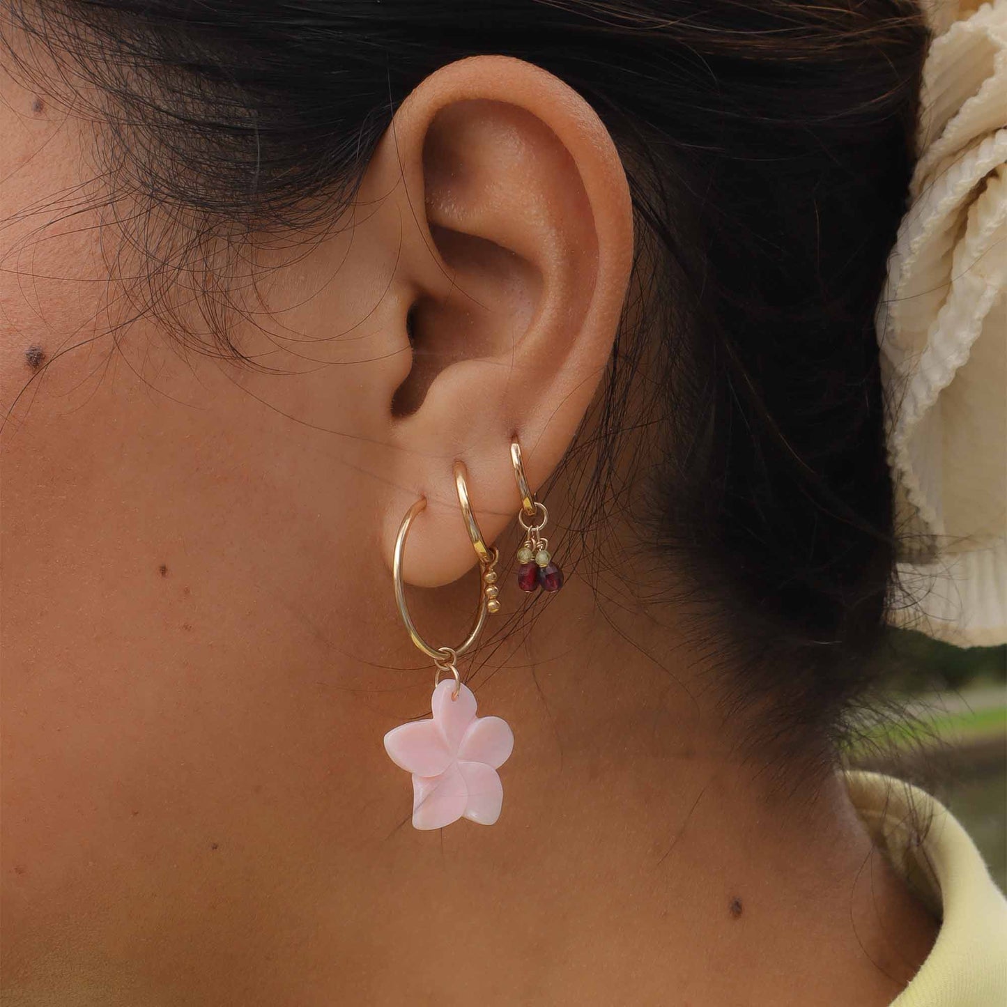 Close-up of an ear wearing gold hoop earrings with pink flower charms.