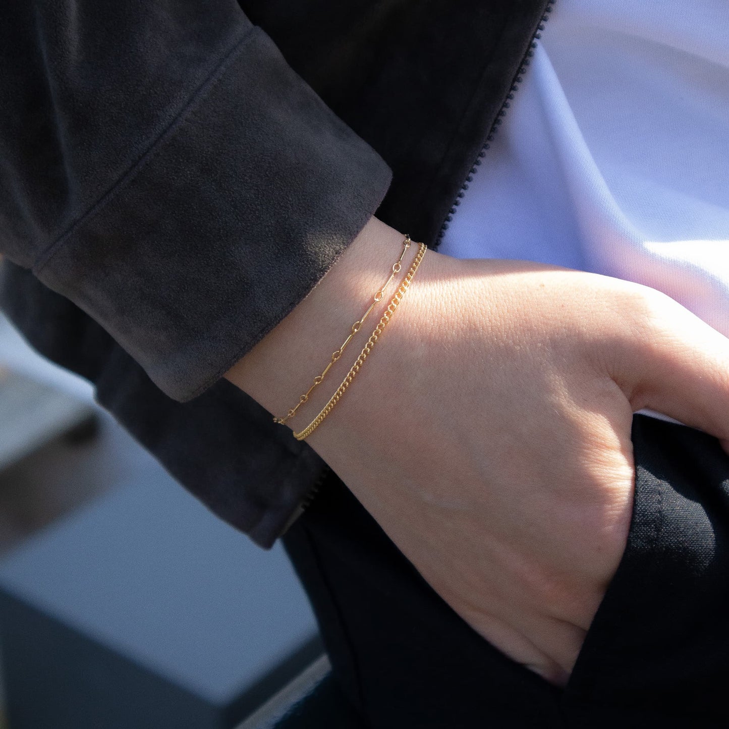 Close-up of a person's wrist wearing a gold bracelet with a blurred background