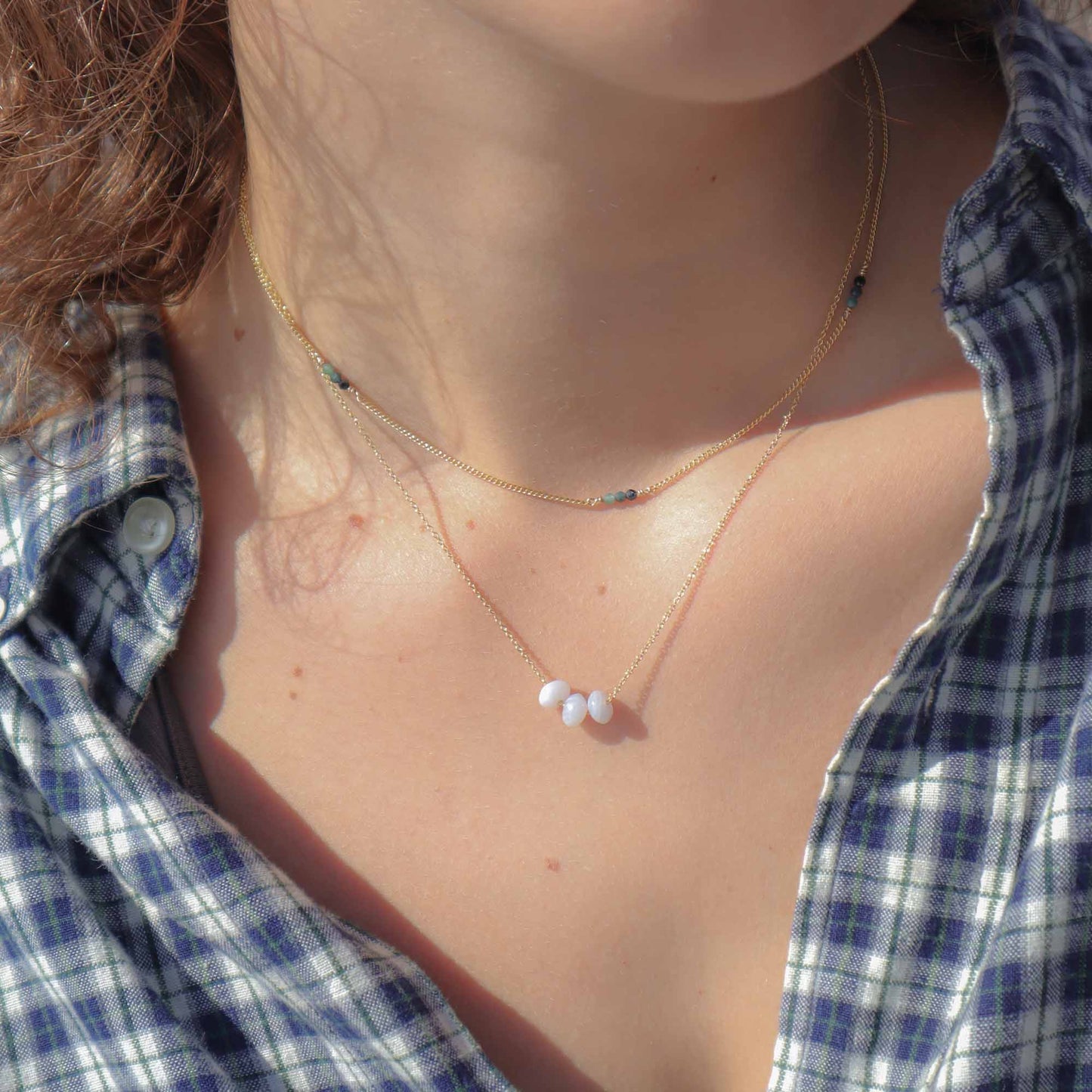 Necklace with small white beads worn by a person in a plaid shirt.
