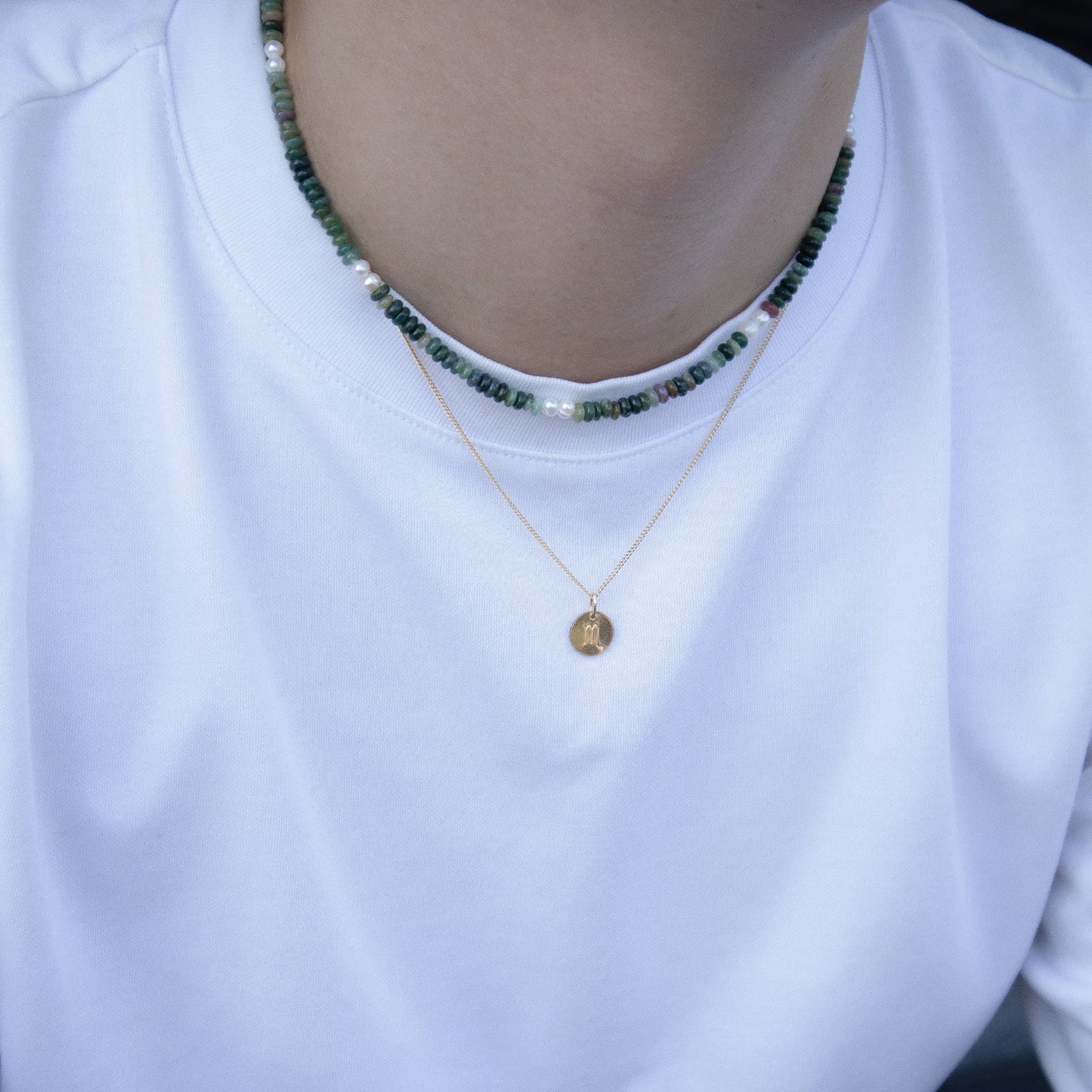 Person wearing a white shirt with a gold necklace and green beaded necklace.