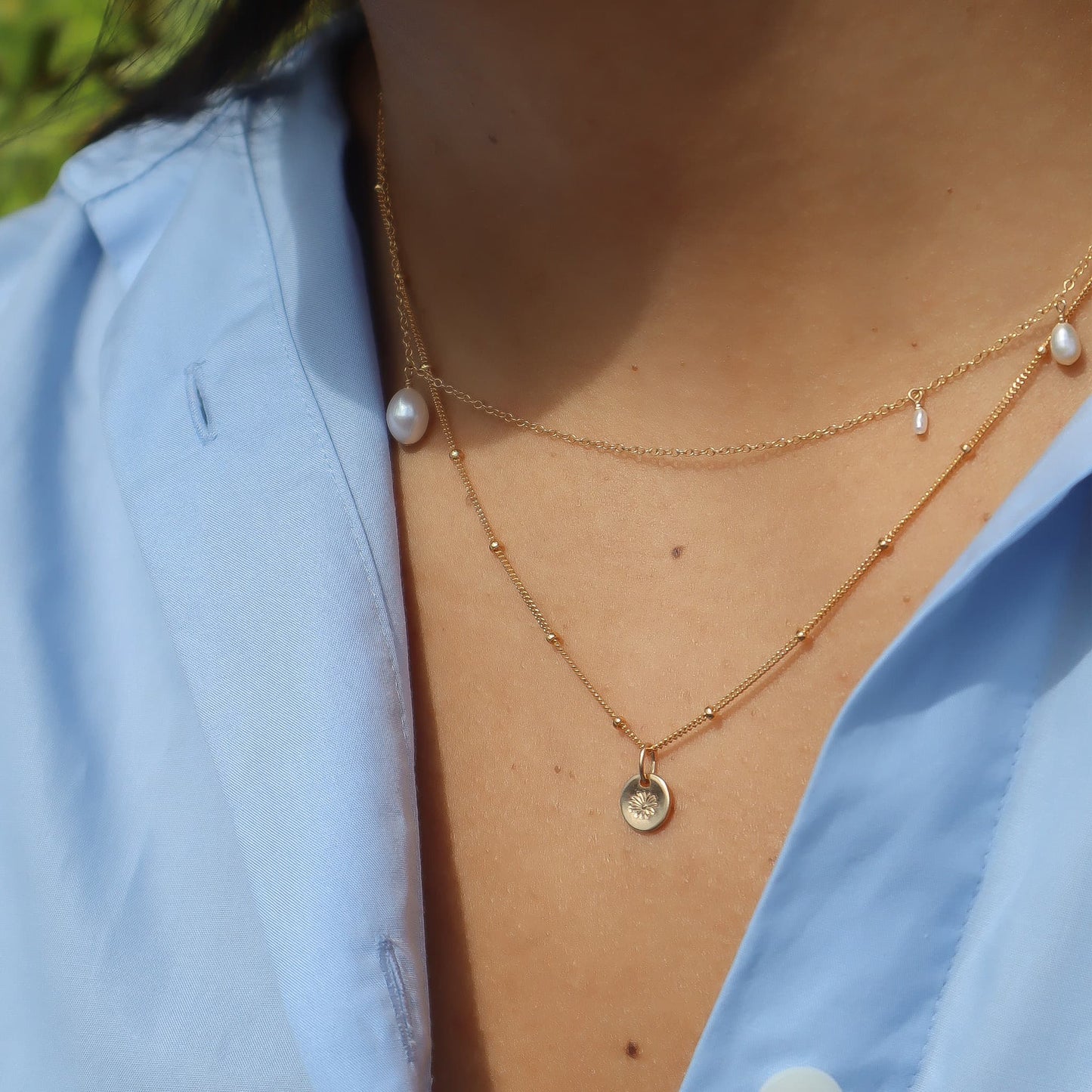 Close-up of a person wearing a gold necklace with pearls and a blue shirt.