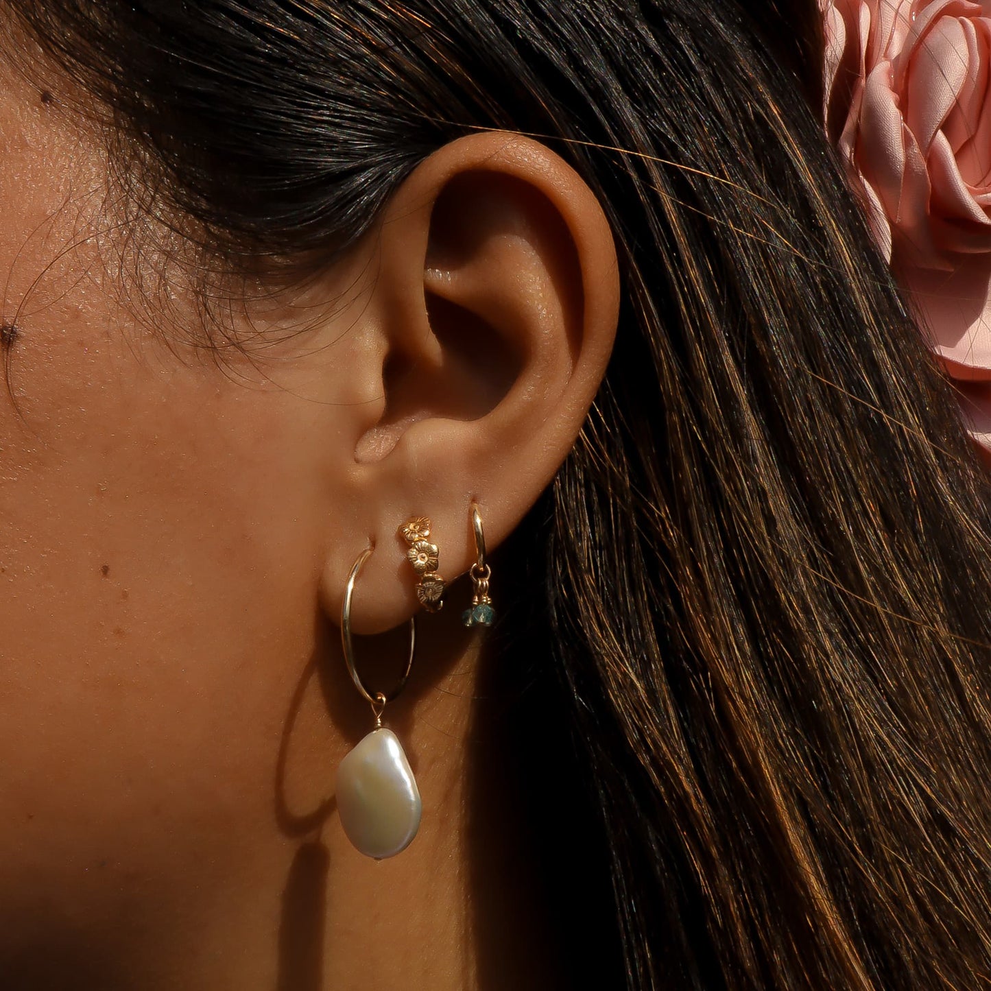 Close-up of an ear with gold hoop earrings and a pink flower in hair