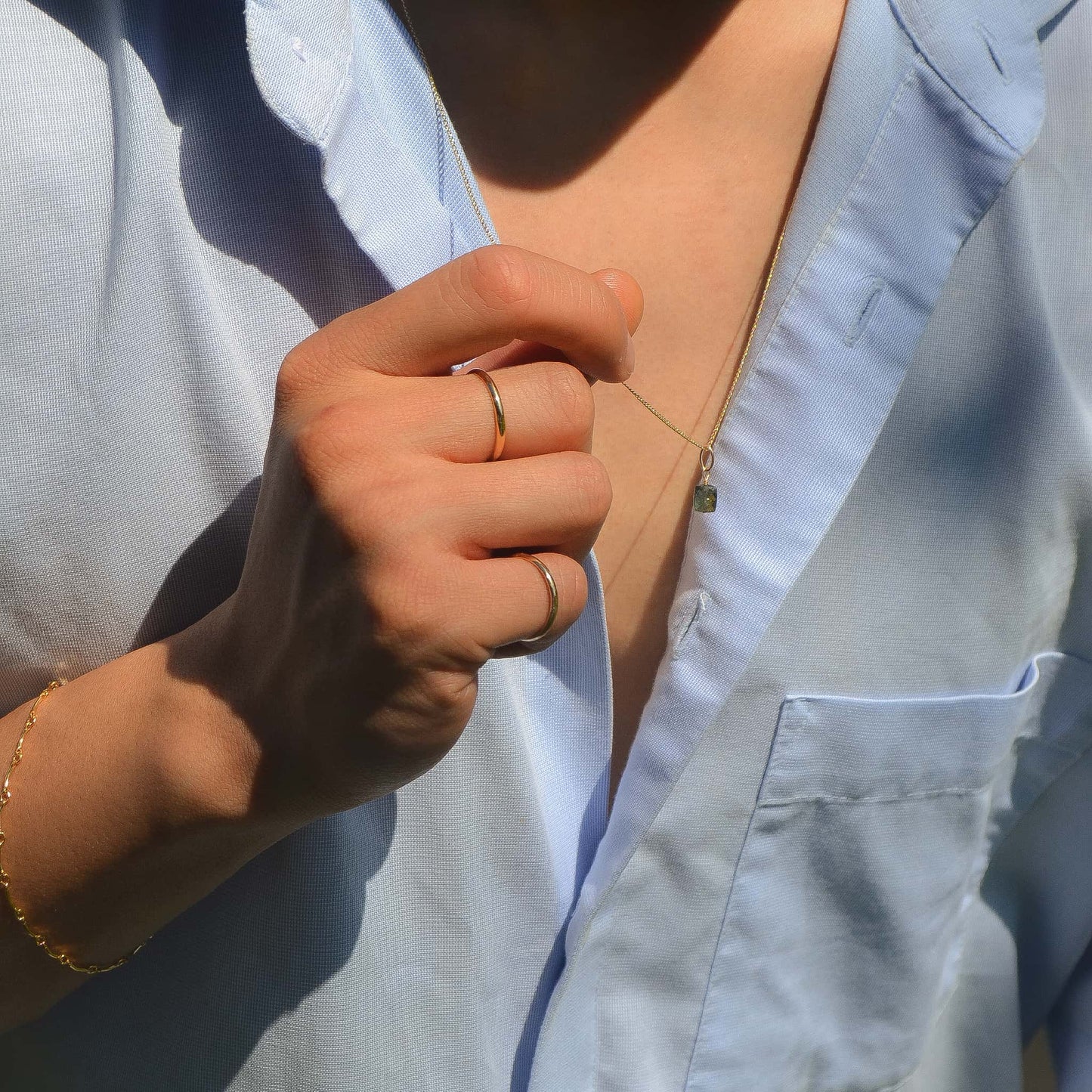 Close-up of a person wearing a light blue shirt with a gold bracelet and rings.
