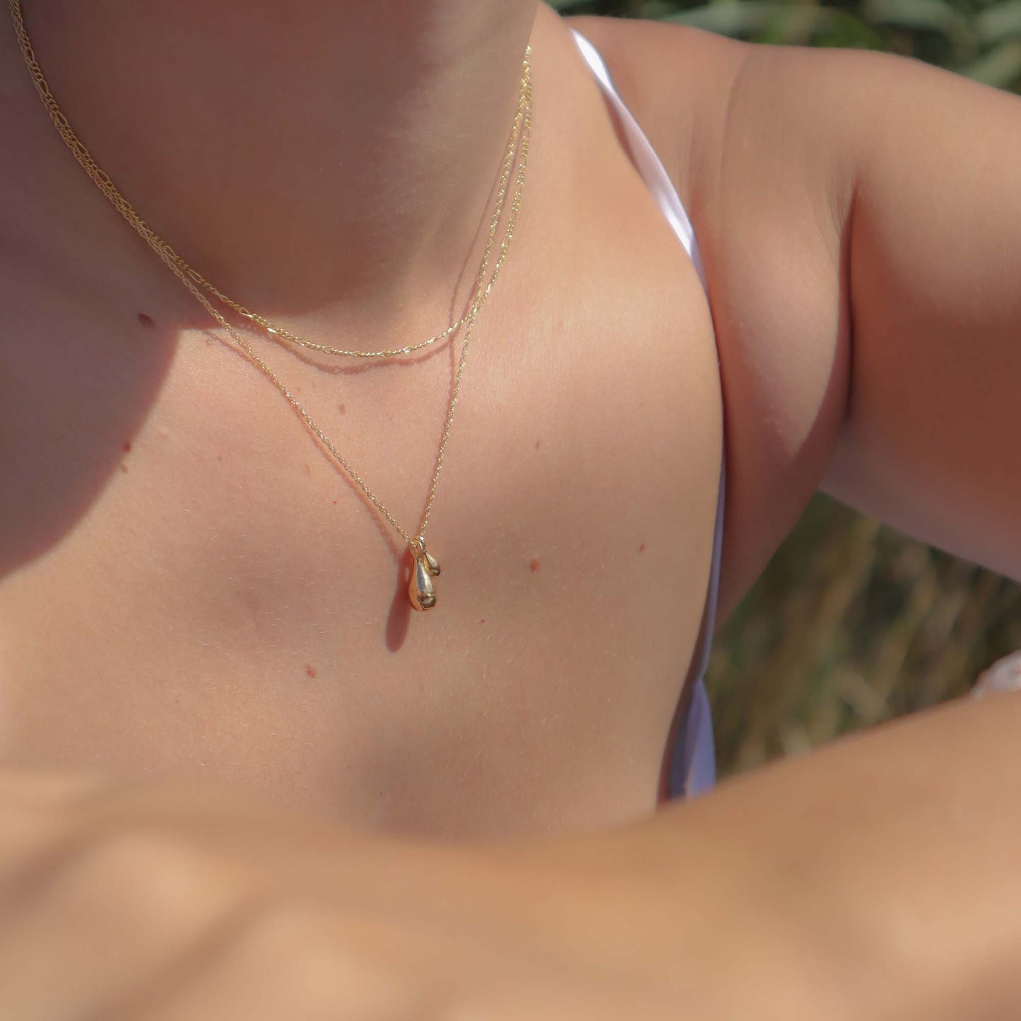 Close-up of a person wearing a gold necklace with a small pendant outdoors.