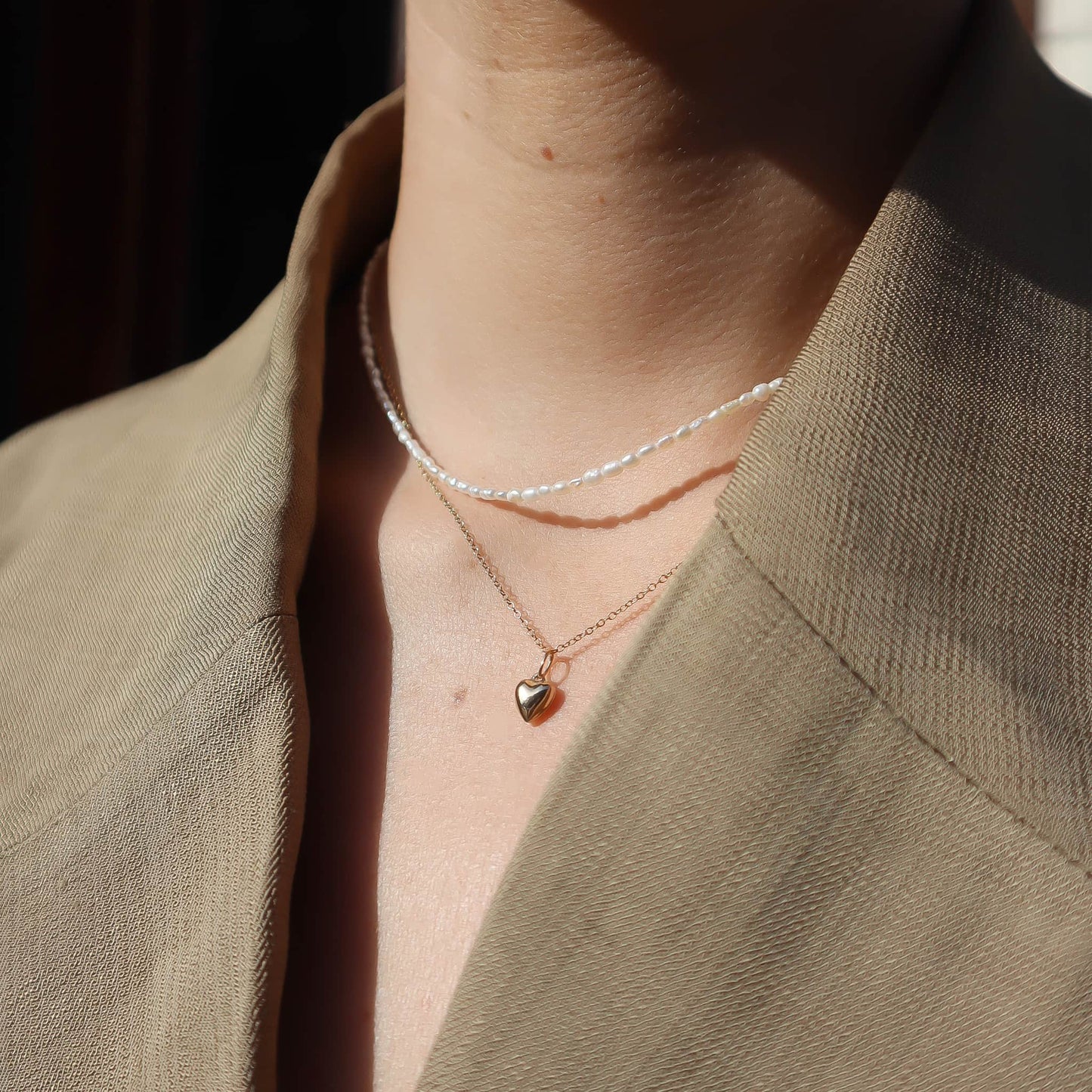 Close-up of a person wearing two necklaces with heart pendants against a neutral background