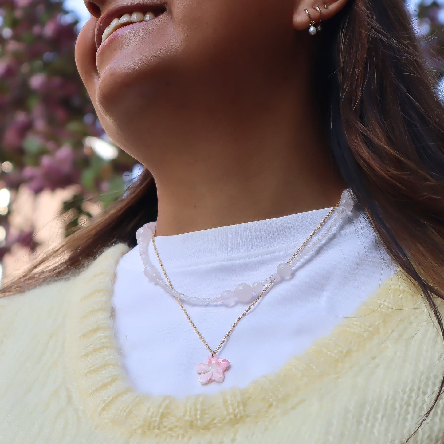 Woman wearing a yellow sweater and white shirt with a pink flower necklace, outdoors.