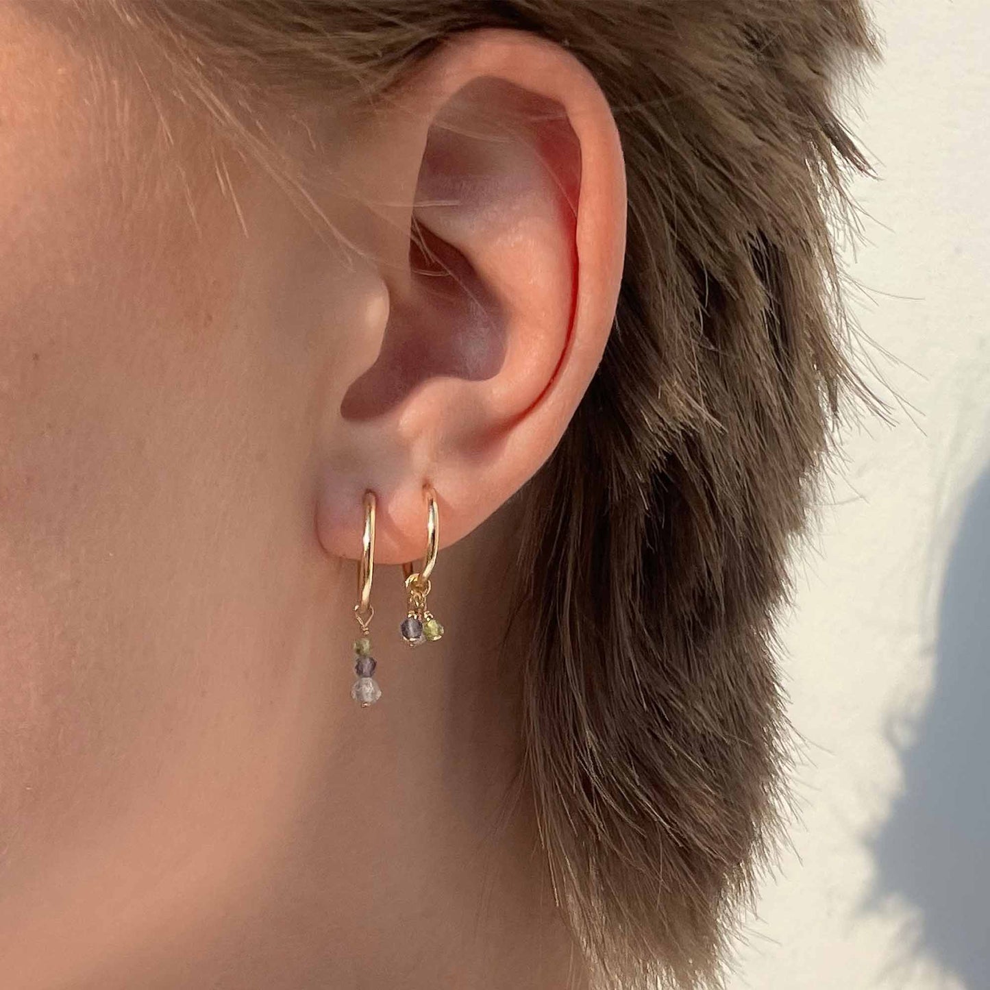 Close-up of an ear wearing gold hoop earrings with small dangling beads.