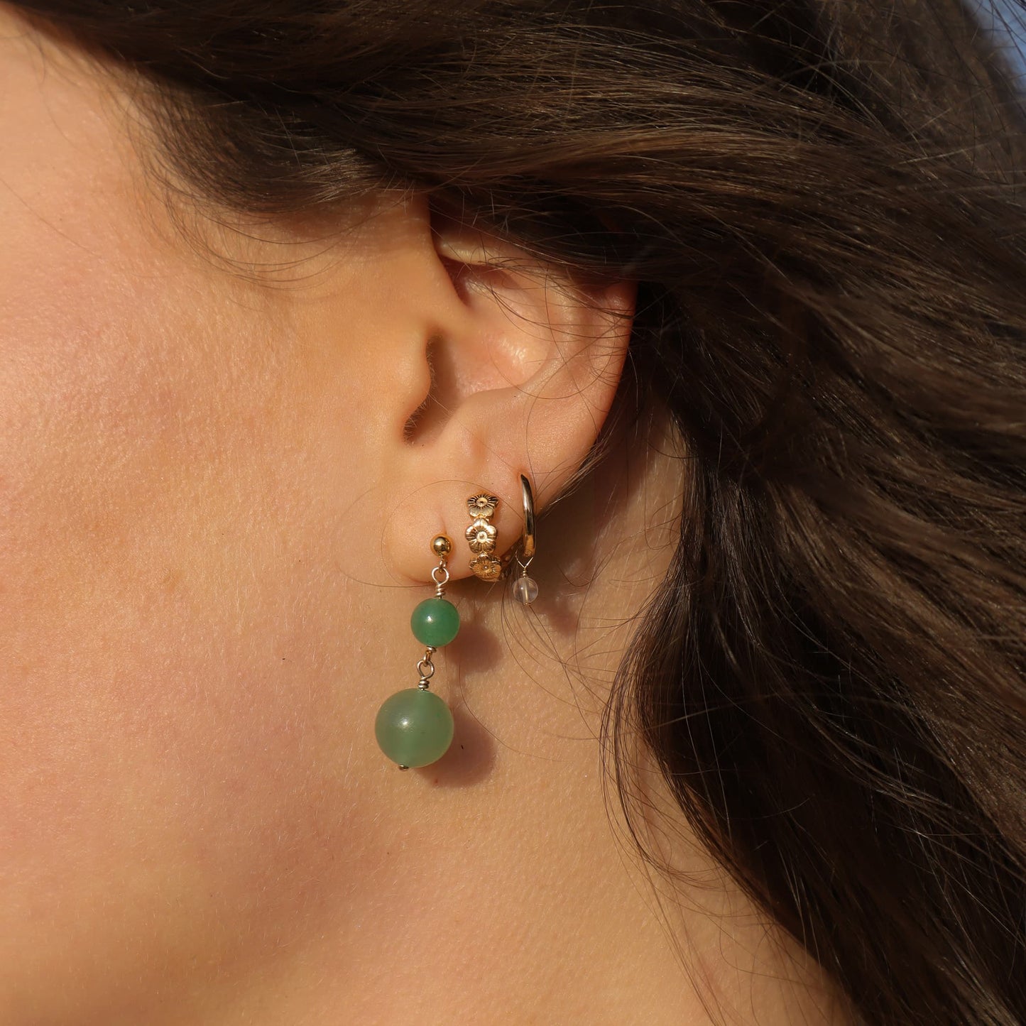 Close-up of an ear wearing gold hoop earrings with green beads.