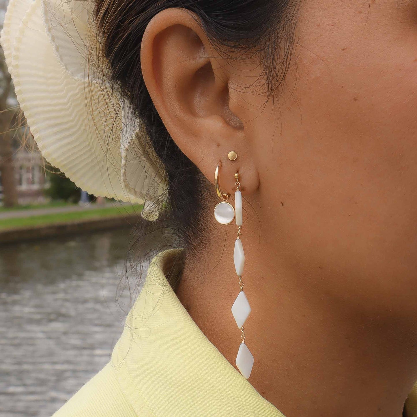 Close-up of a person wearing gold and white earrings with a blurred background
