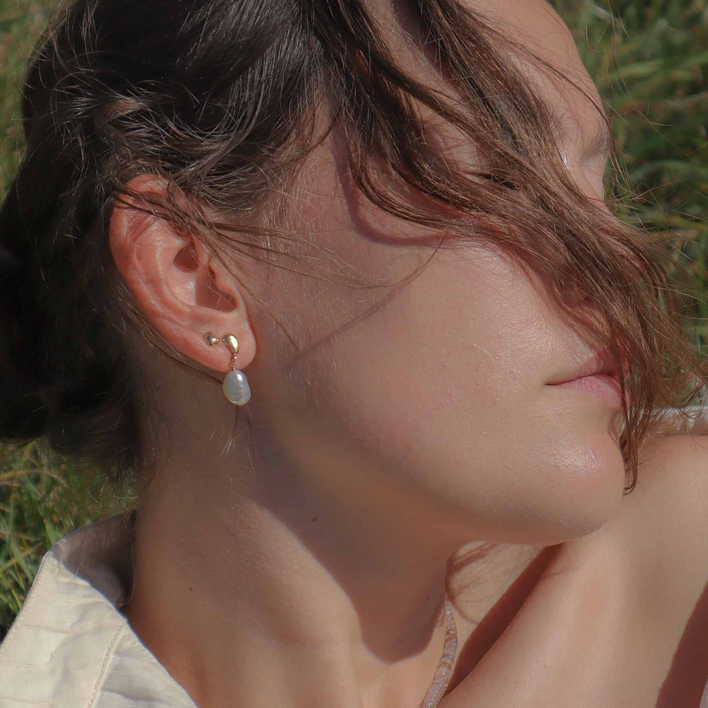 Close-up of a person wearing pearl earrings with a blurred natural background