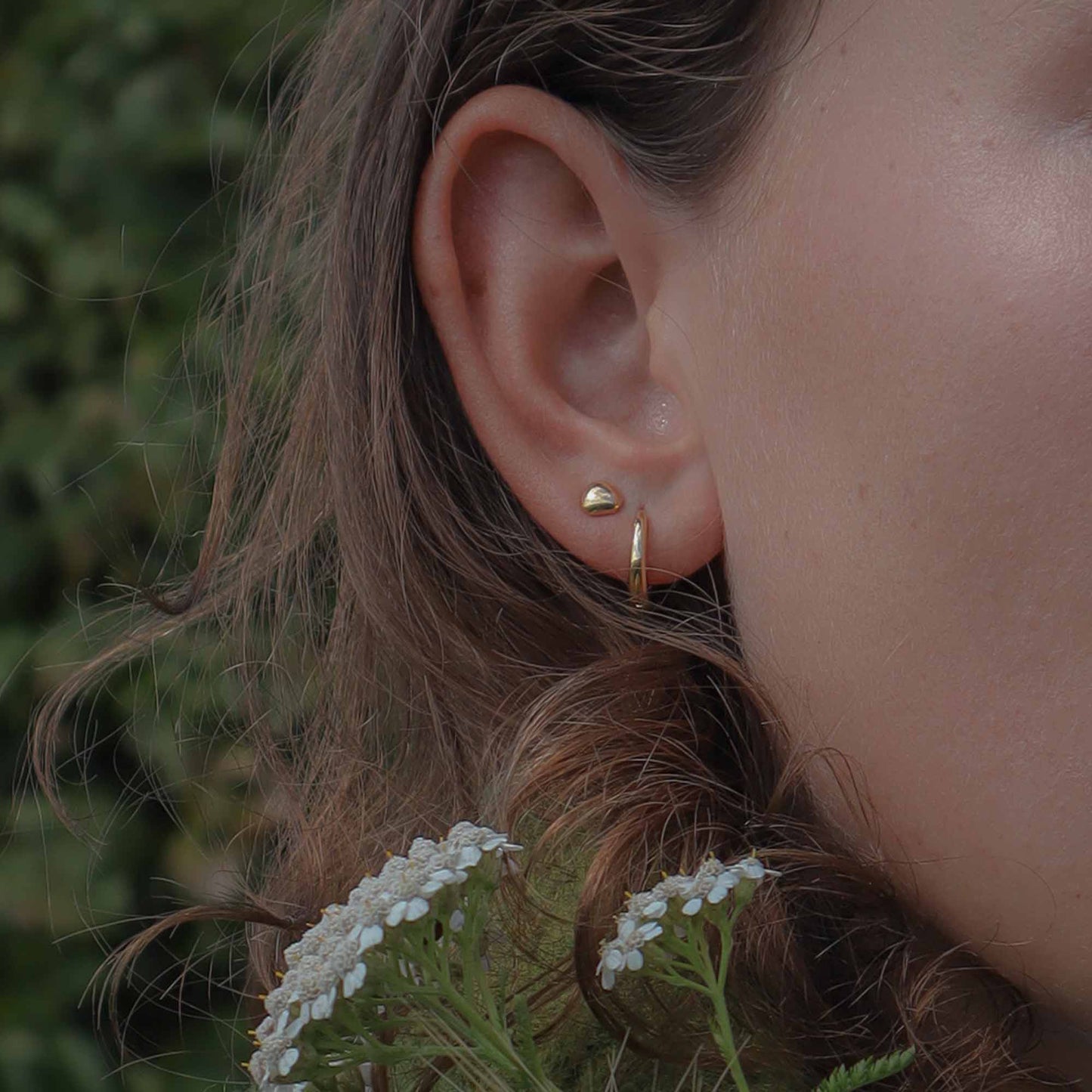 Close-up of an ear wearing a gold hoop earring with a blurred natural background