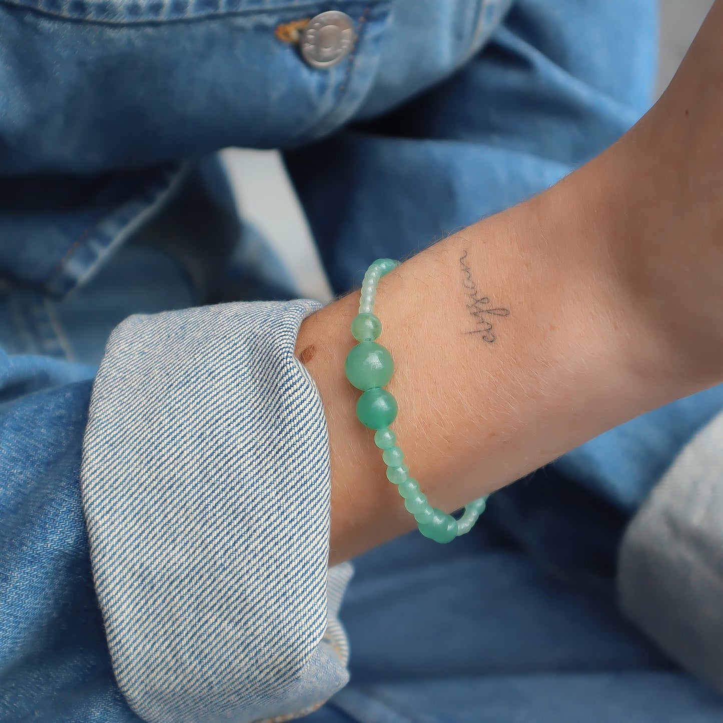 Person wearing a green beaded bracelet on a blue denim background