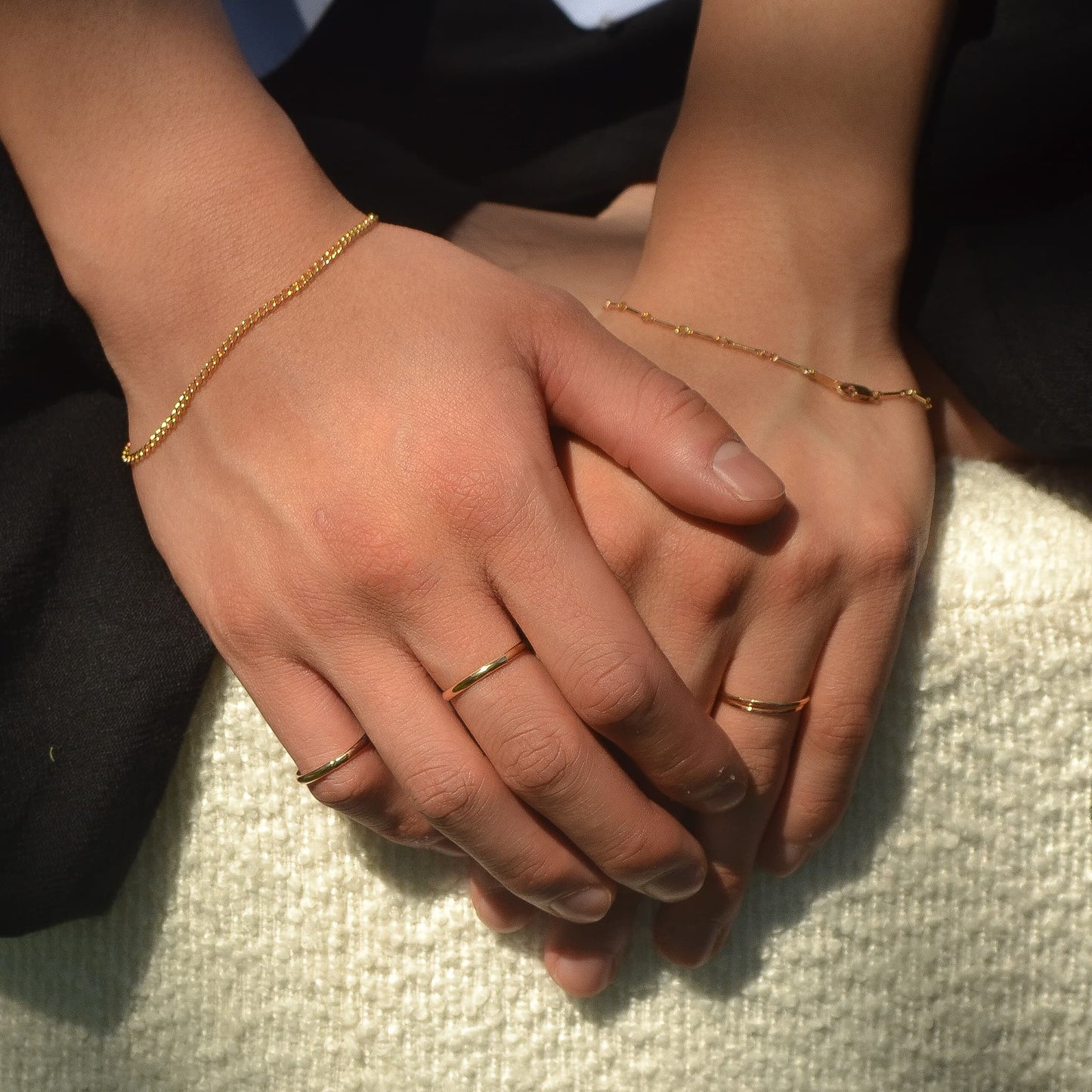 Close-up of two hands holding each other with gold bracelets and rings.