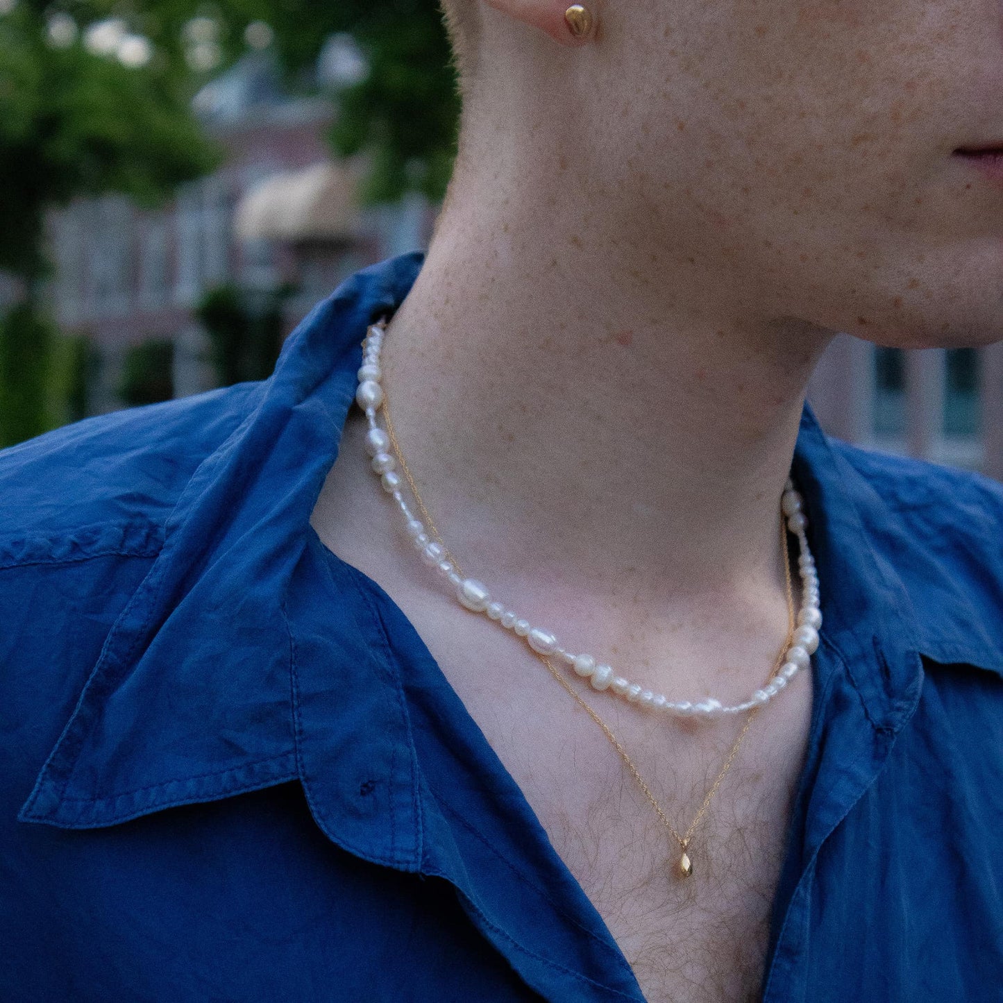 Person wearing a pearl necklace and blue shirt with blurred background