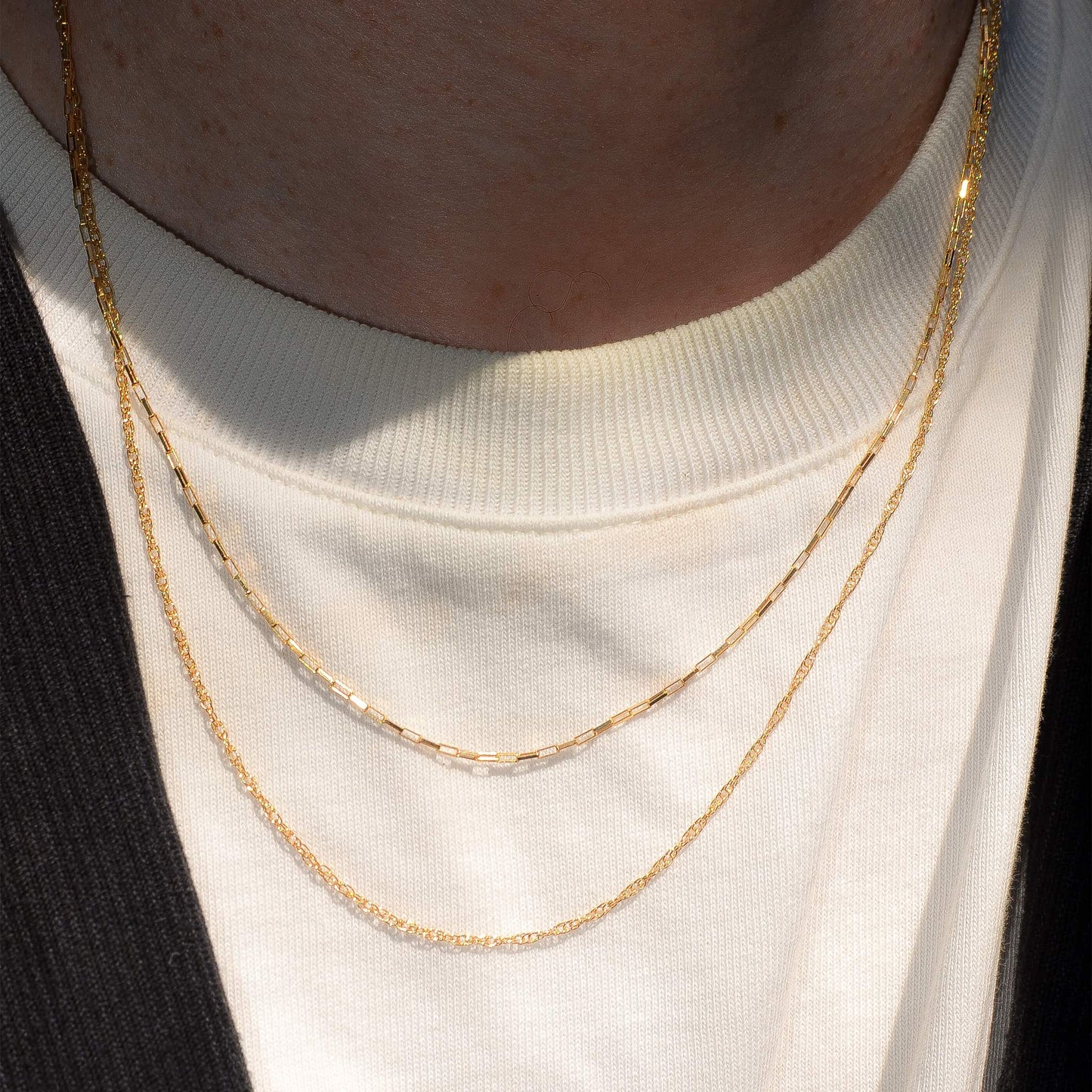 Two gold necklaces on a person wearing a white shirt.