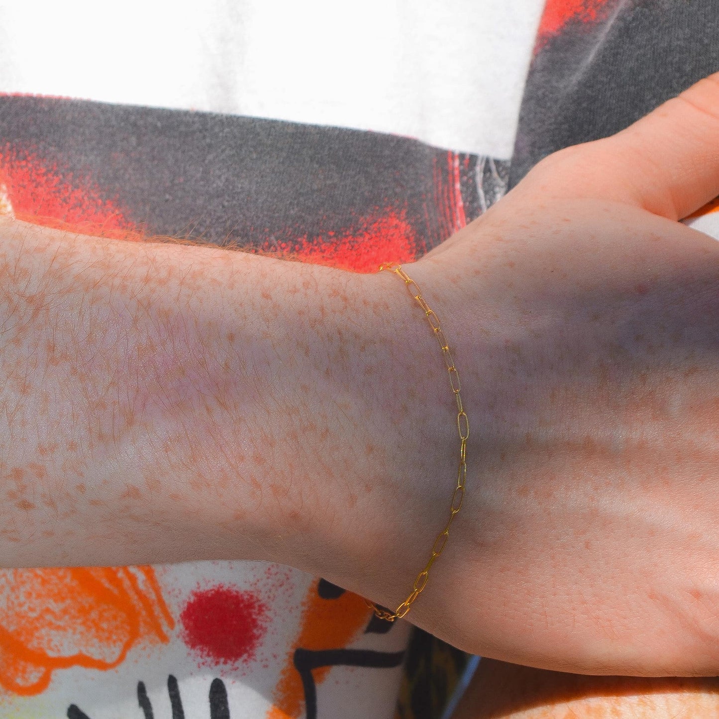 Close-up of a hand wearing a gold bracelet with a colorful background