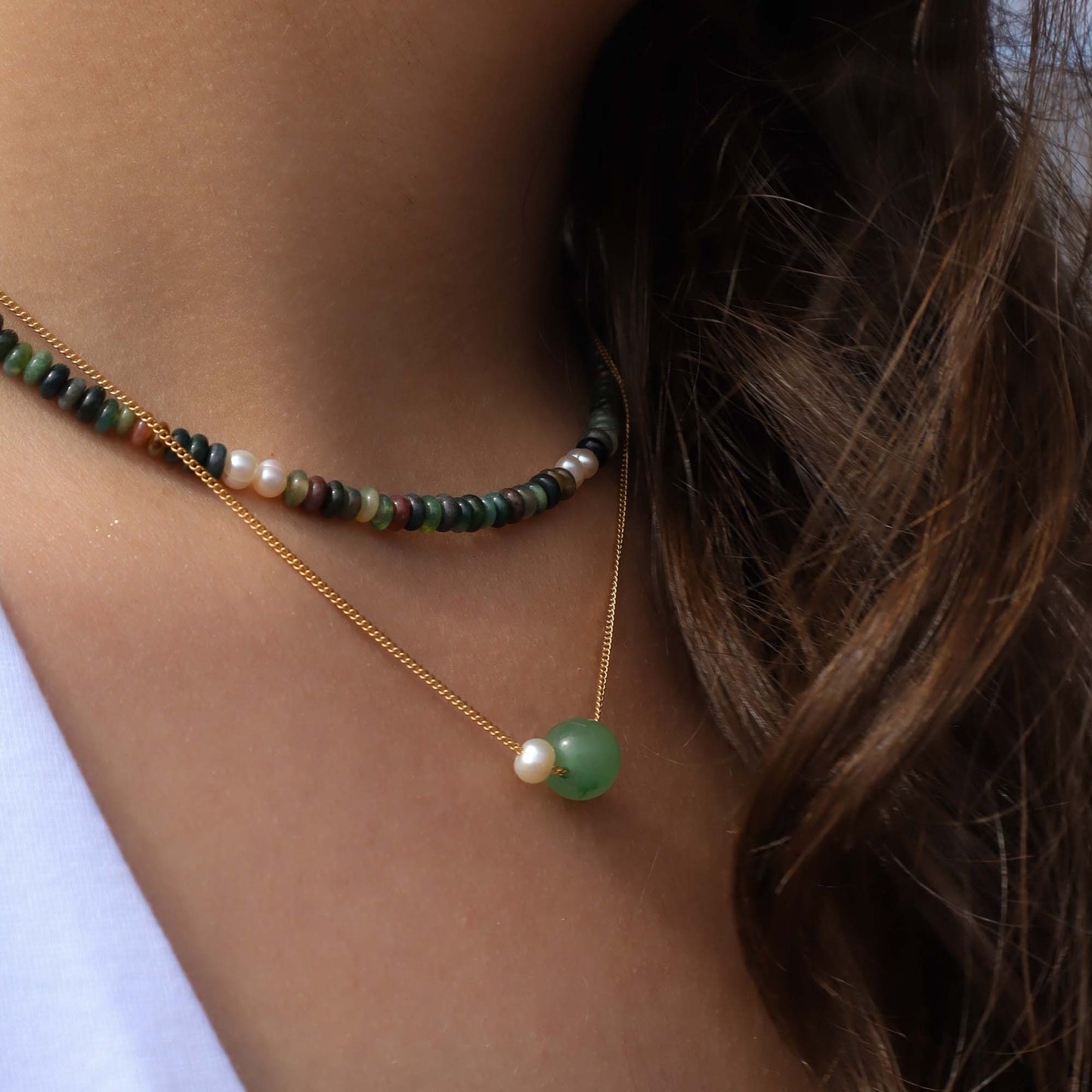 Close-up of a person wearing two necklaces with green and gold beads.