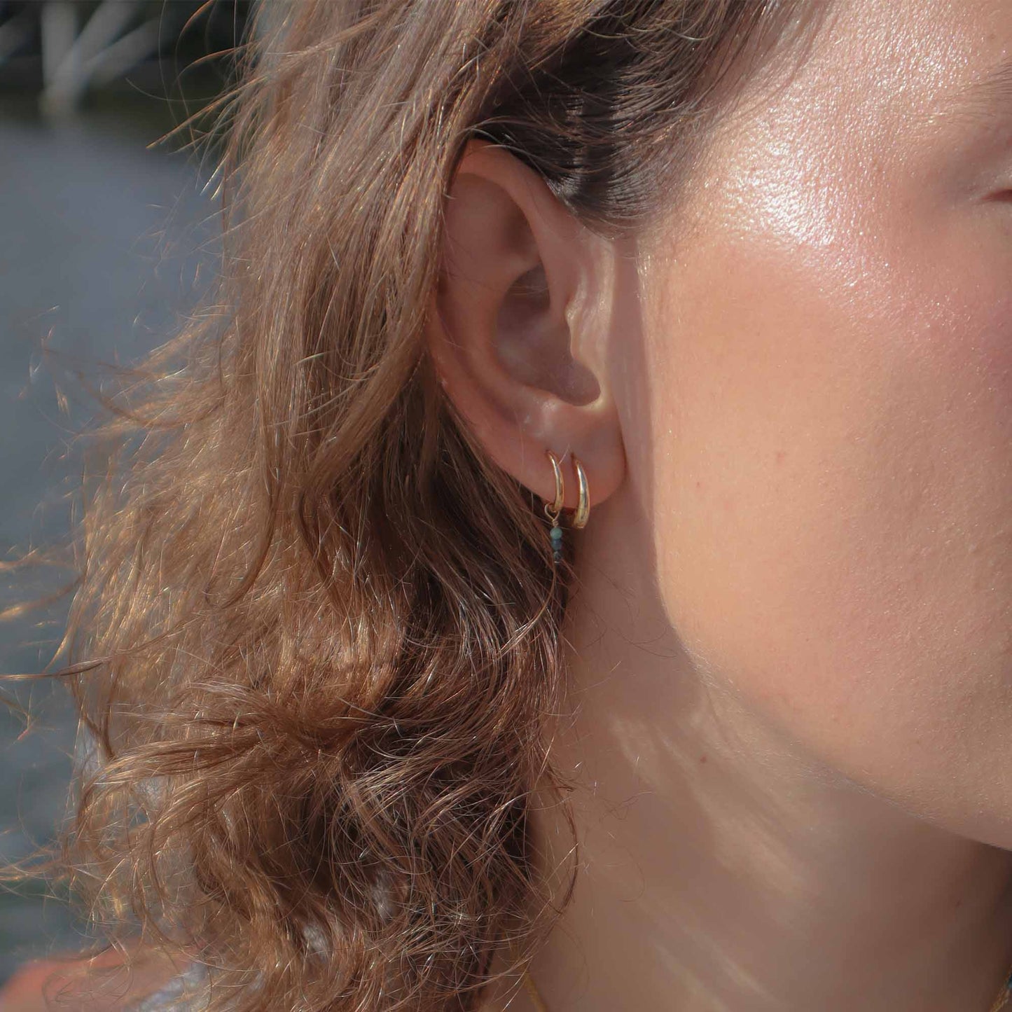 Close-up of a person wearing a gold hoop earring with a blurred background
