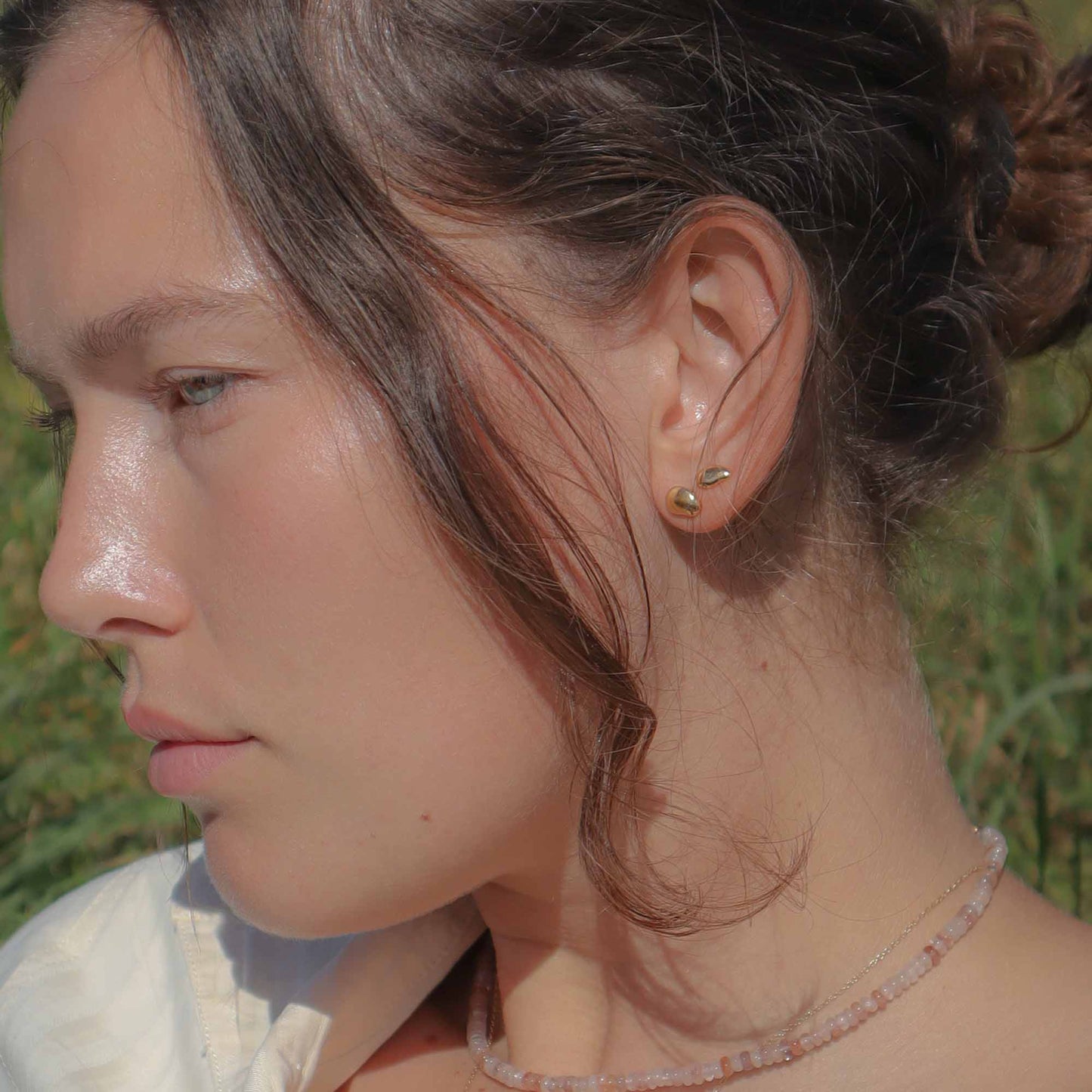 Close-up of a person with a bun and earring in a natural setting