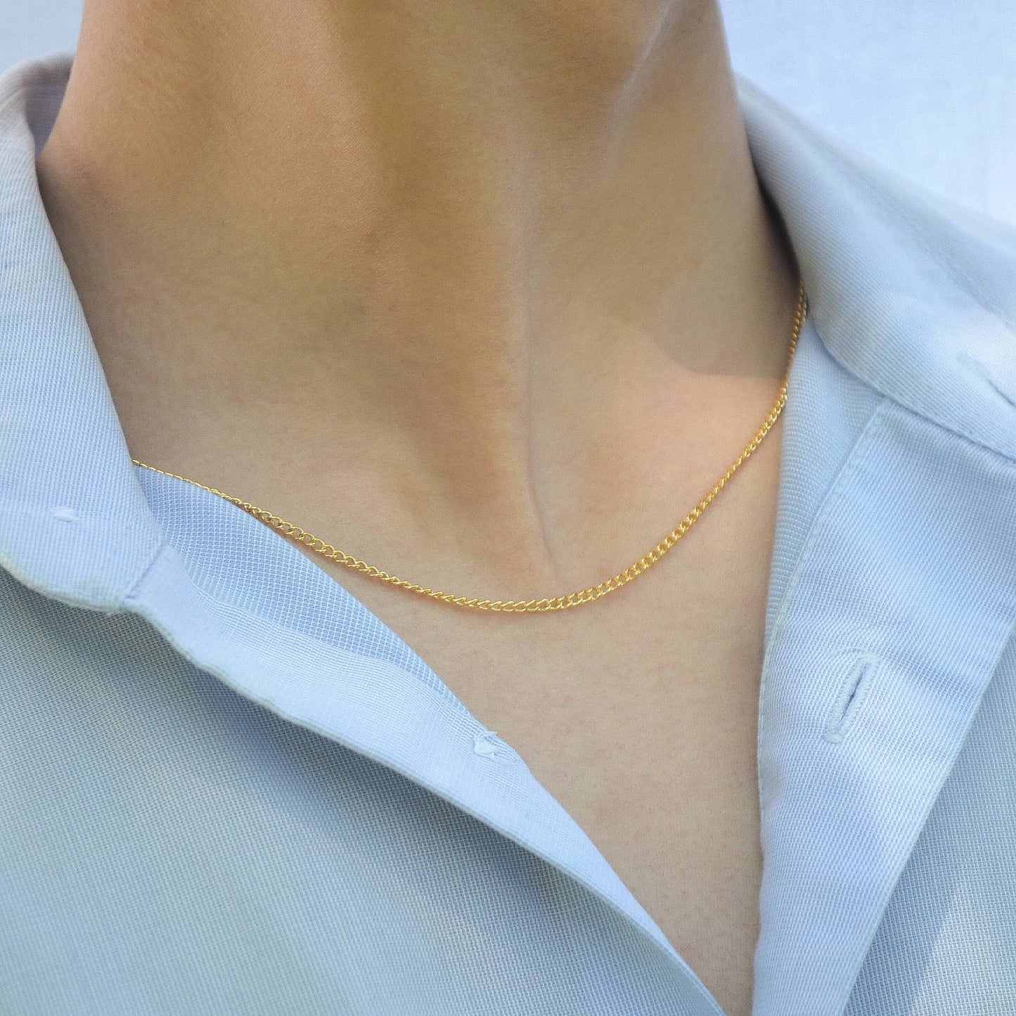 Gold necklace worn by a person with a light blue shirt
