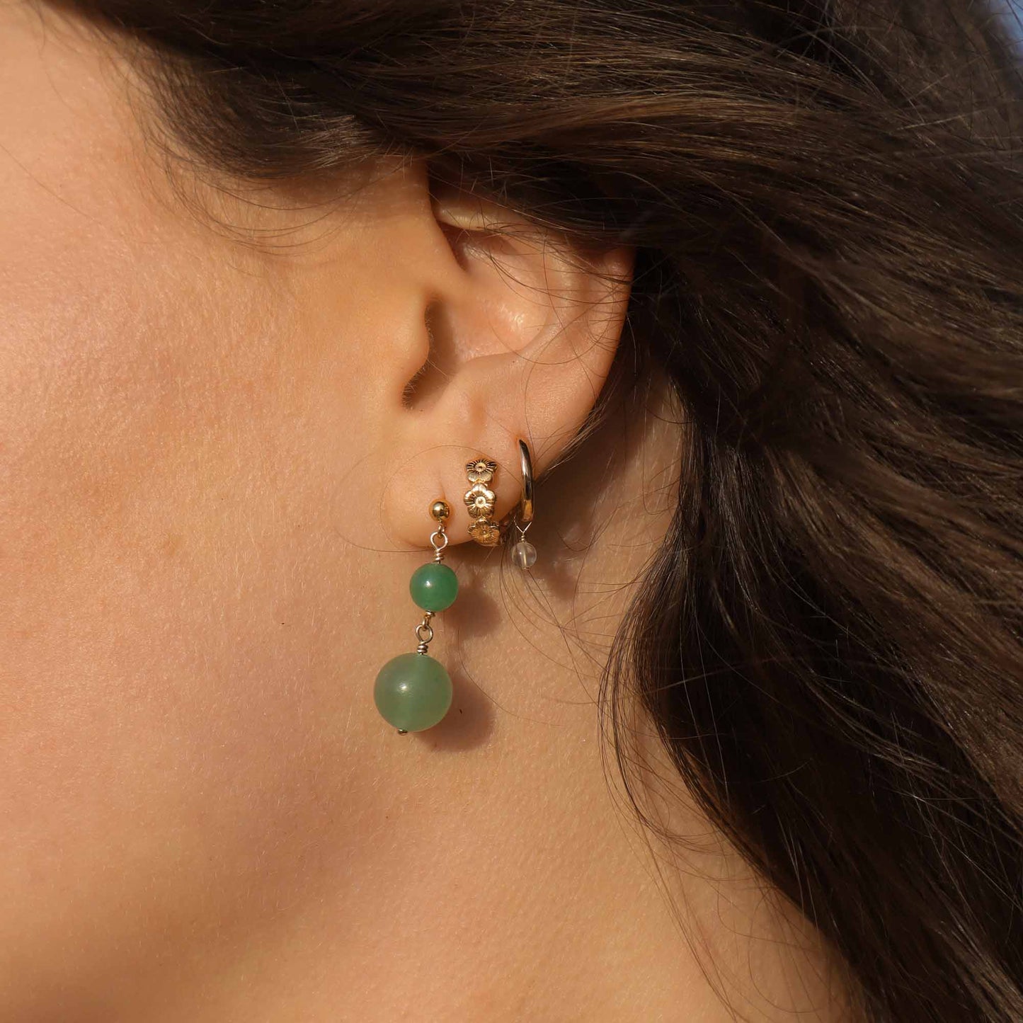 Close-up of an ear wearing gold hoop earrings with green beads.