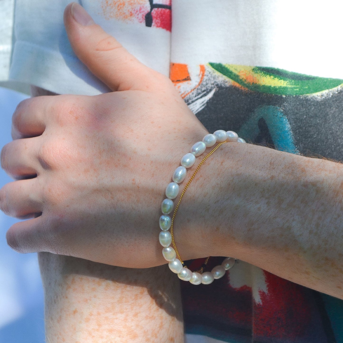 Hand wearing a pearl bracelet with colorful fabric in the background