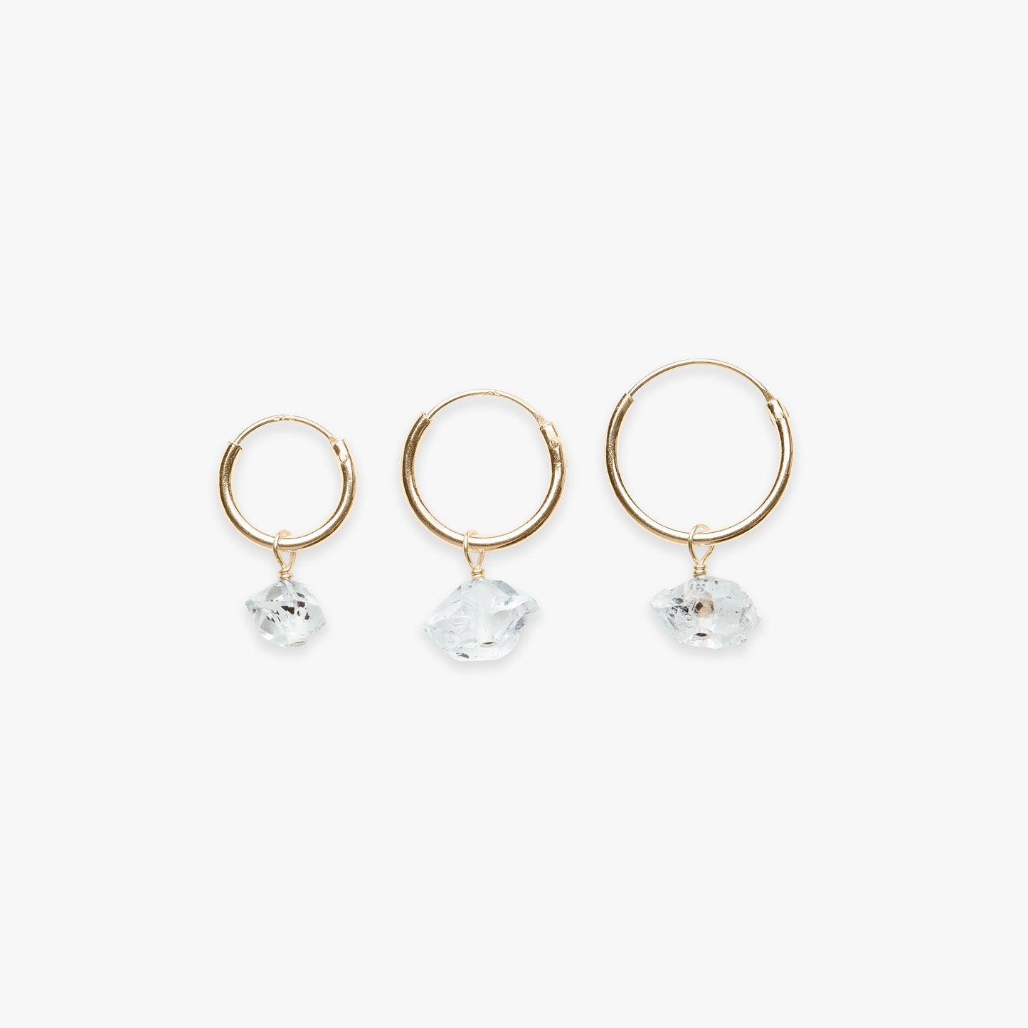 Three gold hoop earrings with clear gemstones on a white background