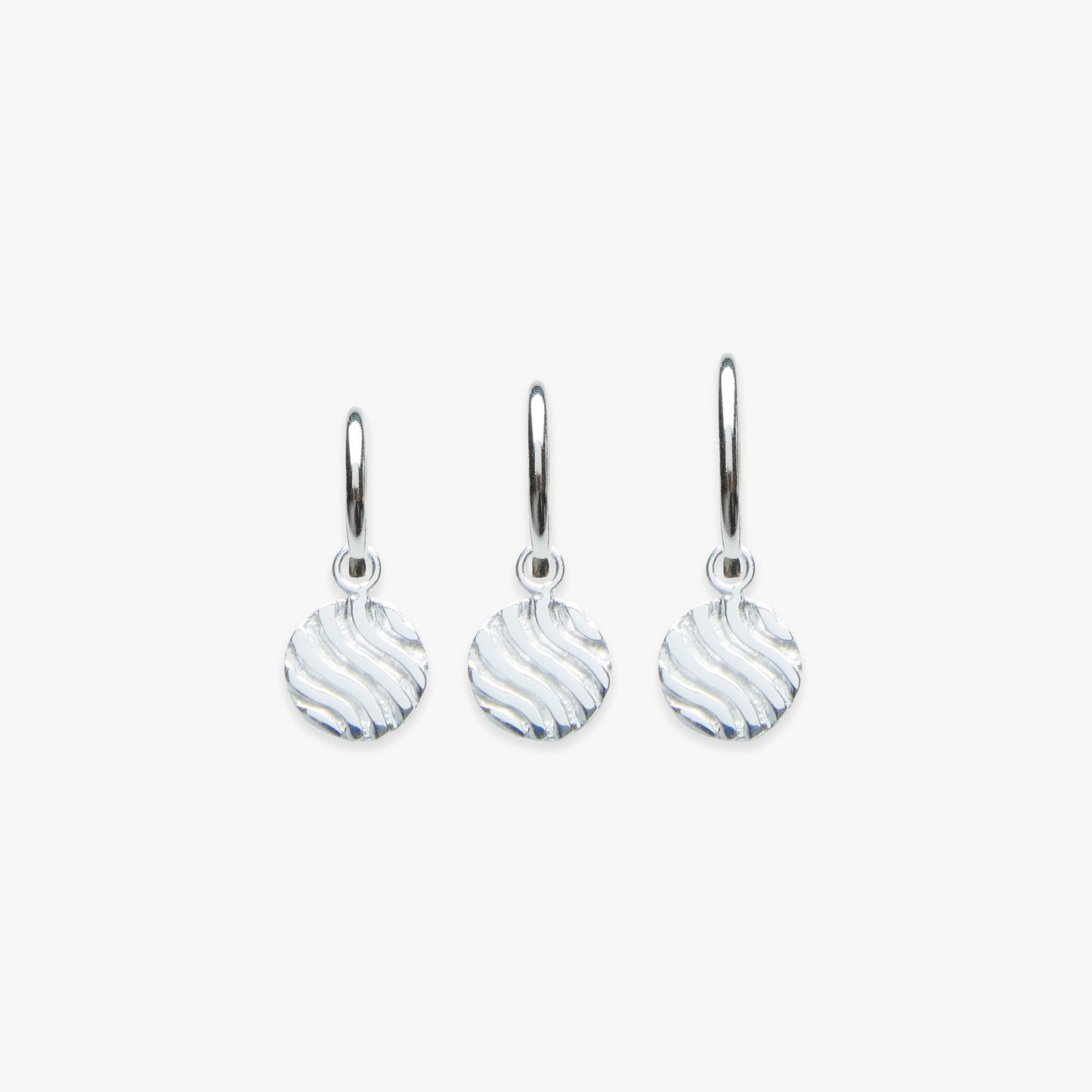 A set of three pendant earrings with a silver finish, featuring a textured design resembling sandy dunes.