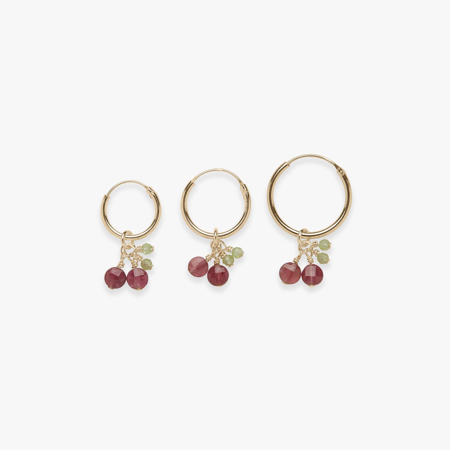 Three gold hoop earrings with cherry gemstone charms on a white background
