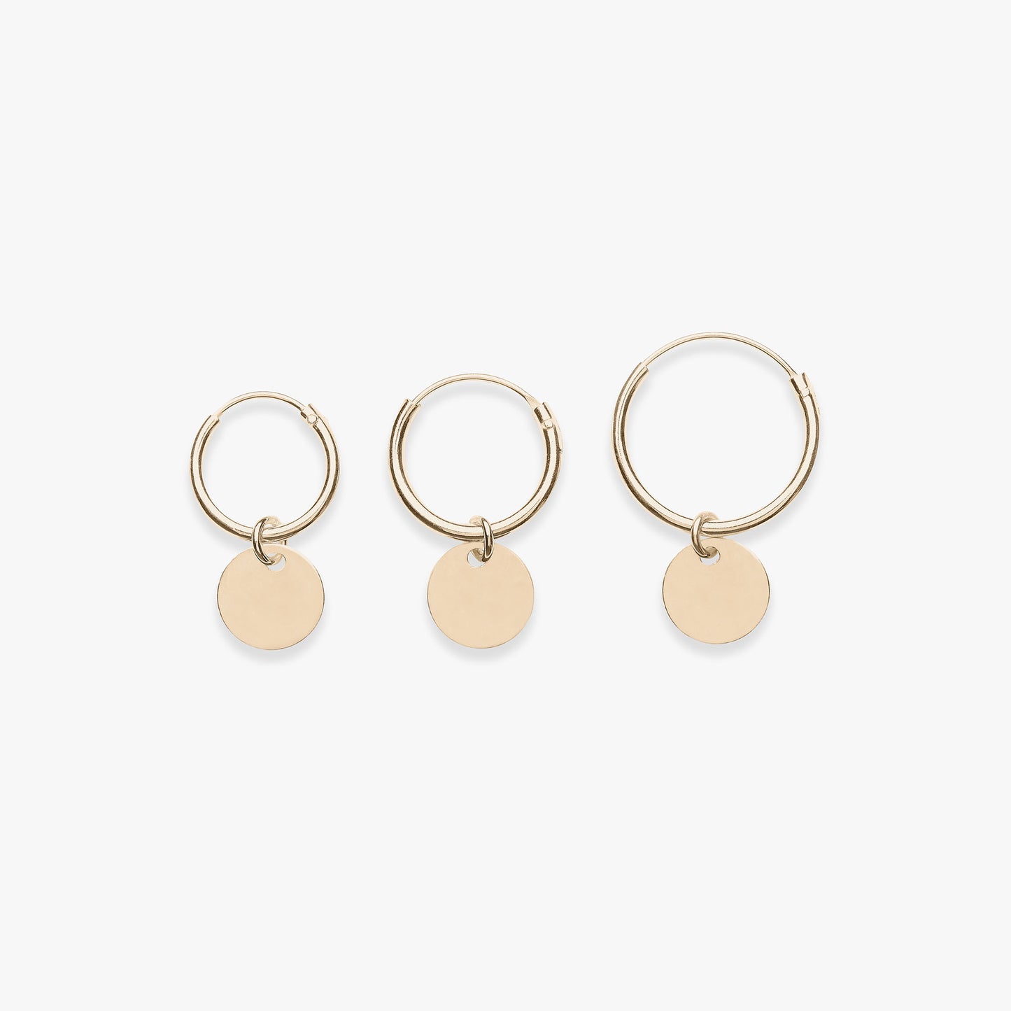 Three gold hoop earrings with round pendants on a white background