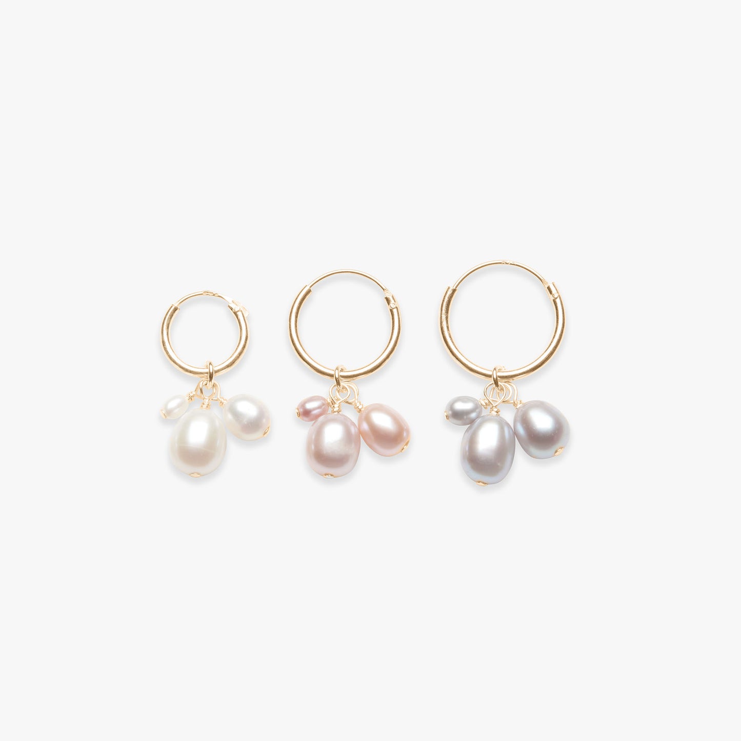 Three pairs of gold hoop earrings with pearl drops on a white background
