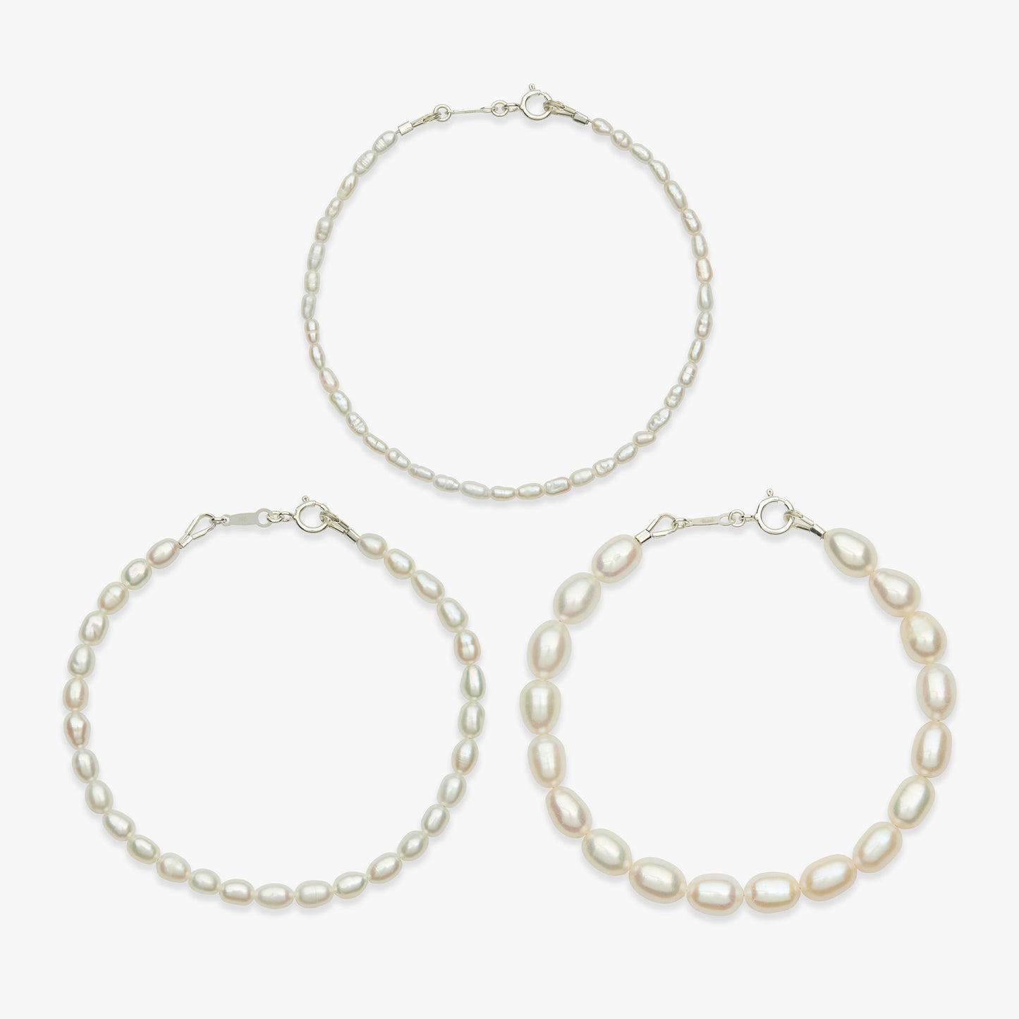 Three pearl jewelry pieces on a light gray background: one delicate chain necklace at the top and two larger pearl bracelets at the bottom left and right.