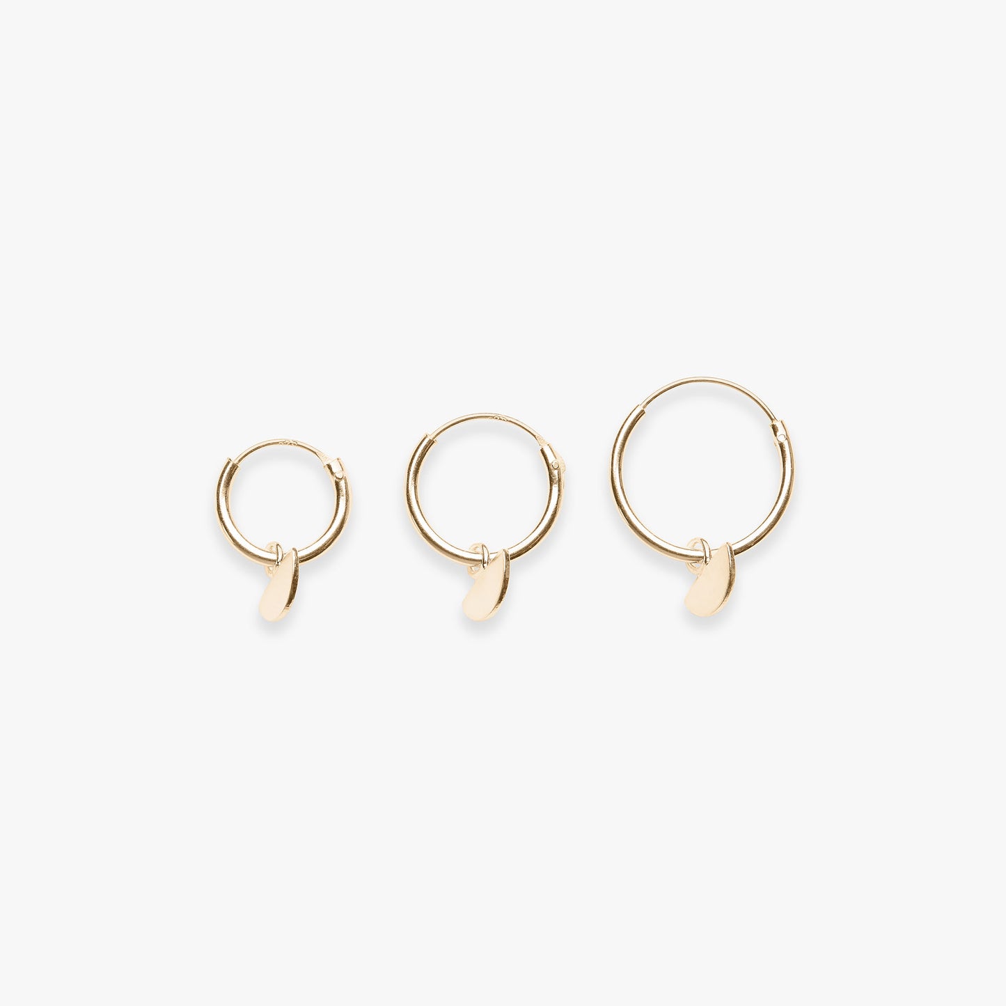 Three gold hoop earrings with small half round pendants on a white background